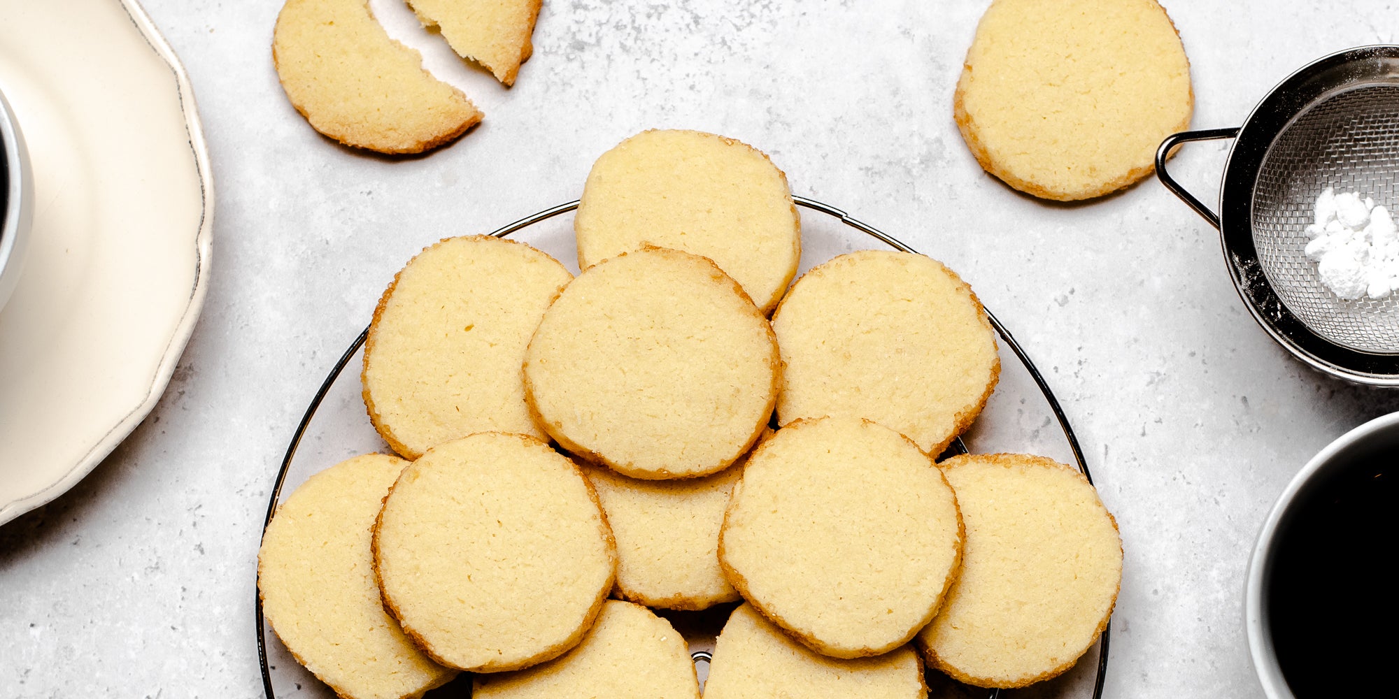 A batch of baked shortbread biscuits on a plate, next to a sieve