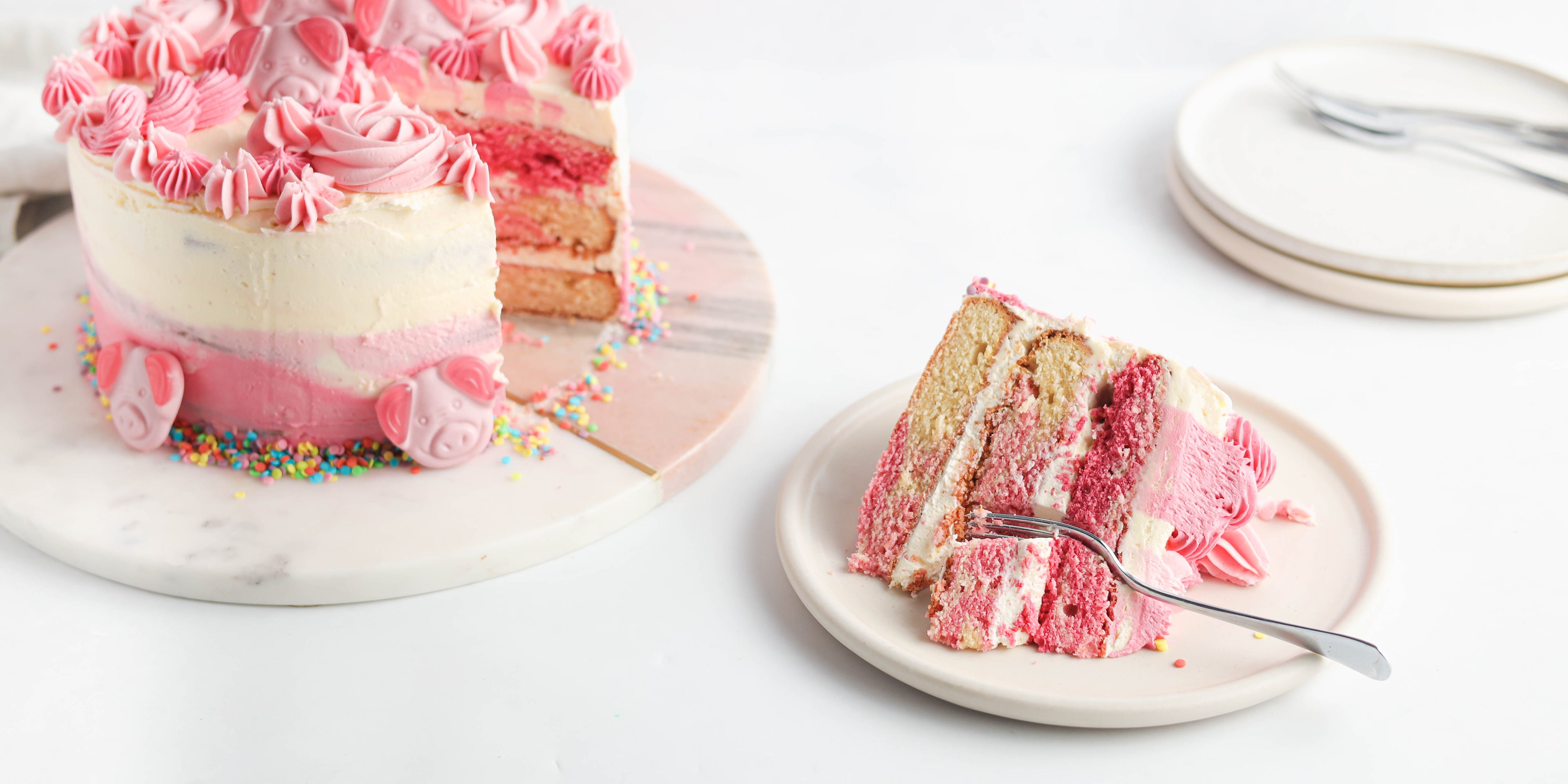 Percy Pig Marble Cake with a slice cut out showing pink ombre layers, decorated with Percy Pig sweets.