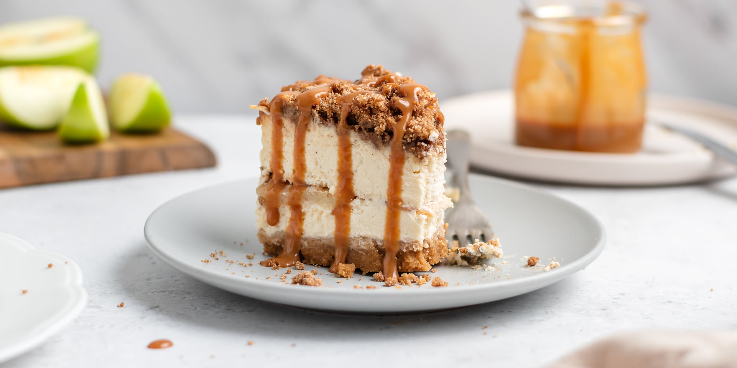 Close up of a slice of Apple Crumble Cheesecake showing the inside layer of finely sliced apples, drizzled with caramel sauce