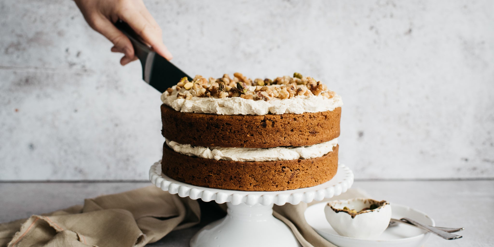 Vegan Carrot Cake being sliced with a hand holding a cake knife, topped with Billington's Golden Icing Sugar and chopped nuts