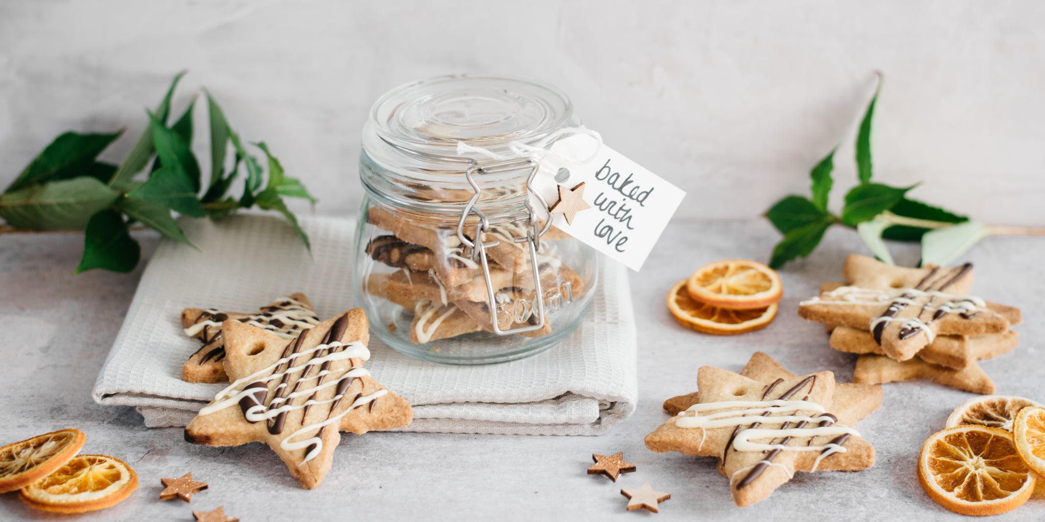 Orange & Ginger shortbread stars in a jar with a hand written note, as a gift at Christmas. Next to sliced orange and star biscuits drizzled in chocolate