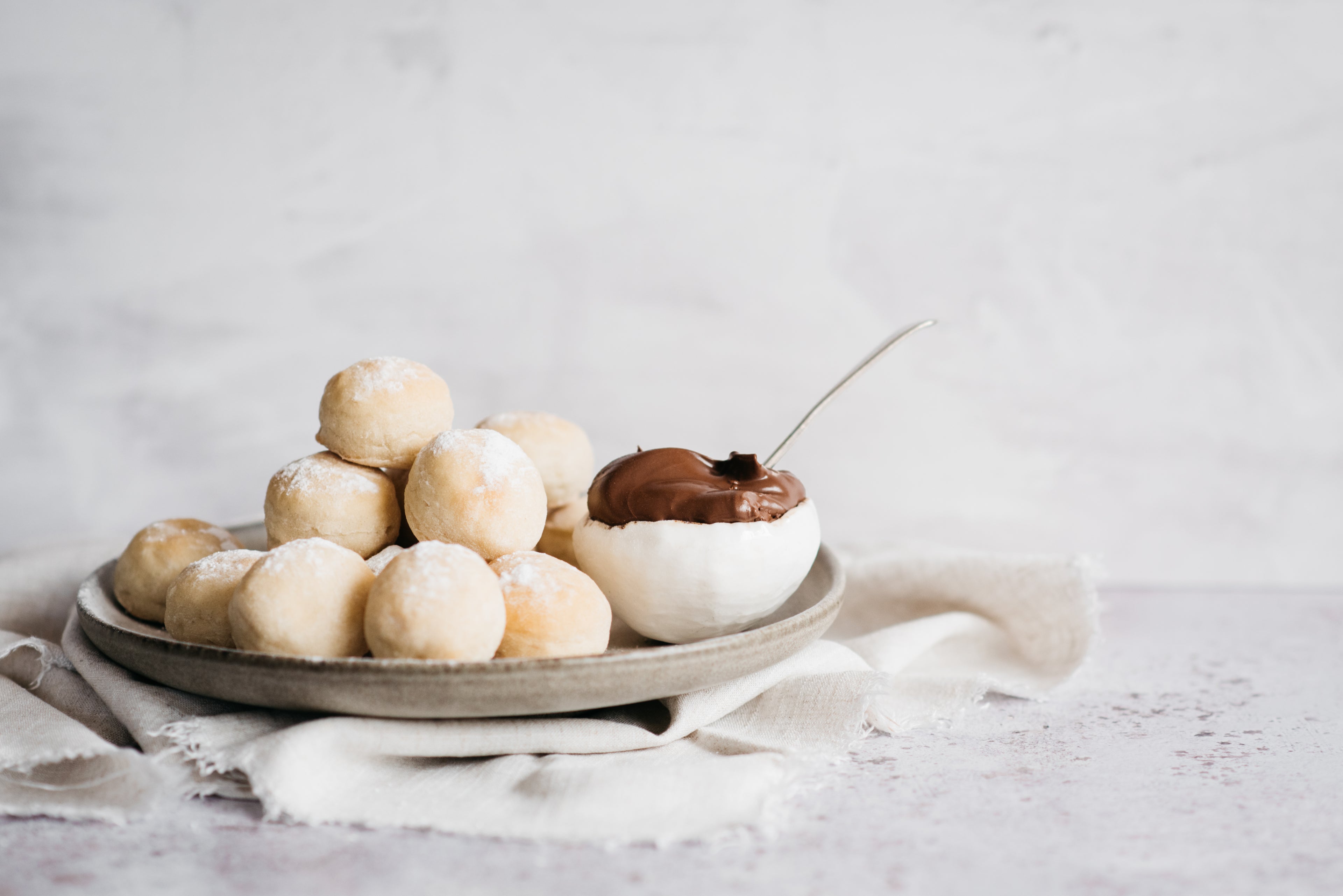 A stack of Chocolate Dough Balls served on a plate, with a bowl of chocolate sauce with a spoon
