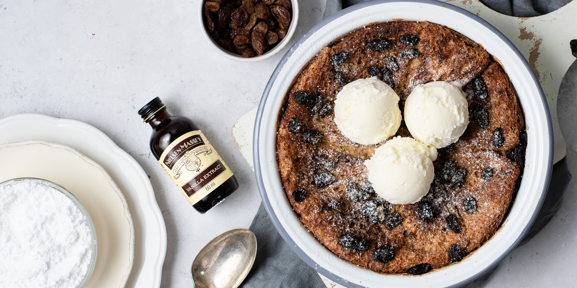 Bread and butter pudding in a bowl with 3 scoops of ice cream on top and vanilla bottle with spoon