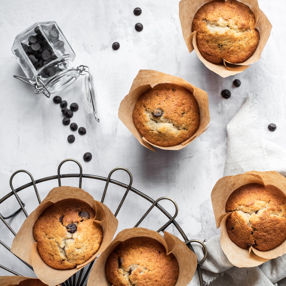 Banana and chocolate chip muffins in brown paper cases shot from above on a wire tray and some on a grey marble surface.