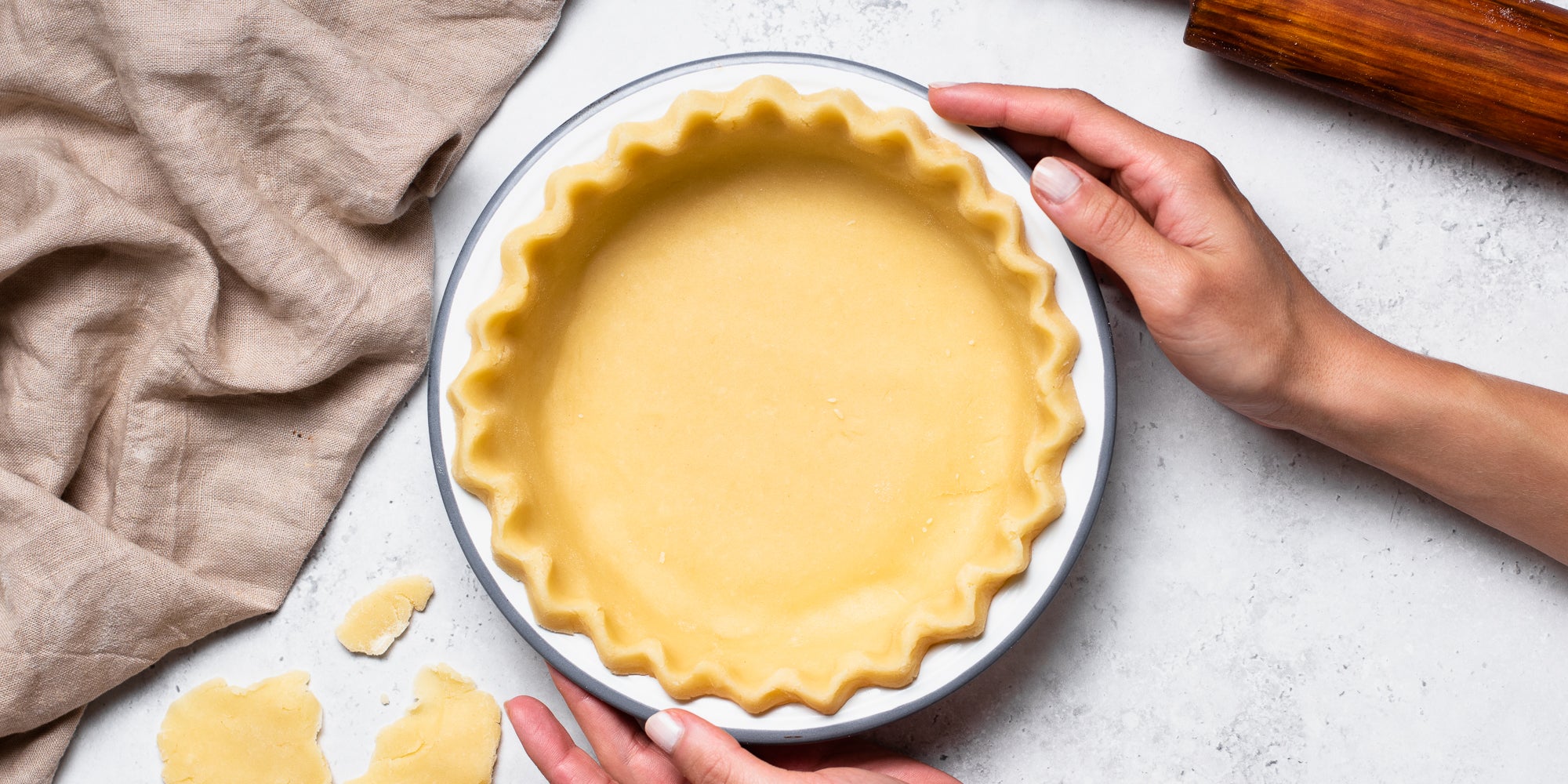 Gently placing homemade shortcrust pastry into a scalloped pie dish