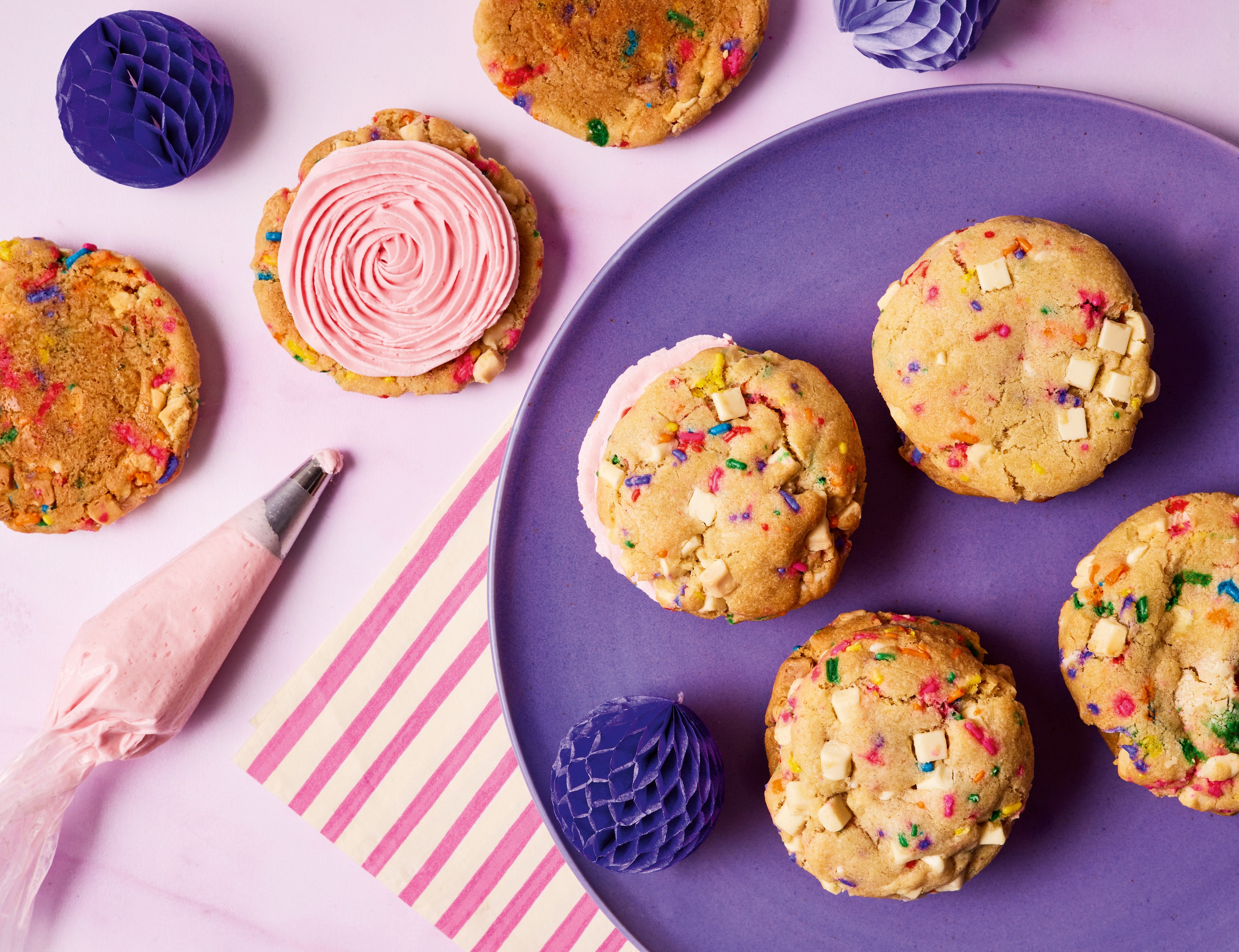 Purple plate with 4 cookies on. Piping bag beside it with a cookie topped with buttercream