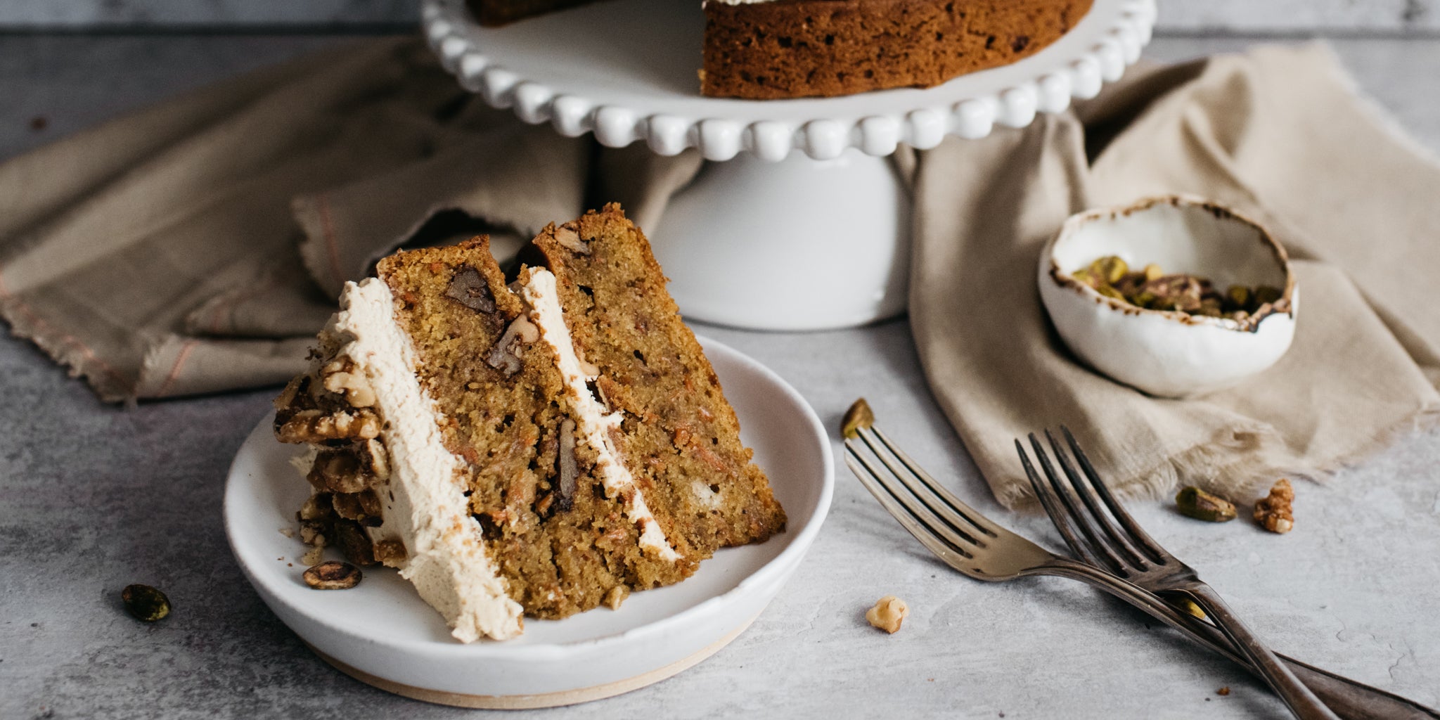 Close up of a slice of Vegan Carrot Cake on a plate, next to forks ready to serve