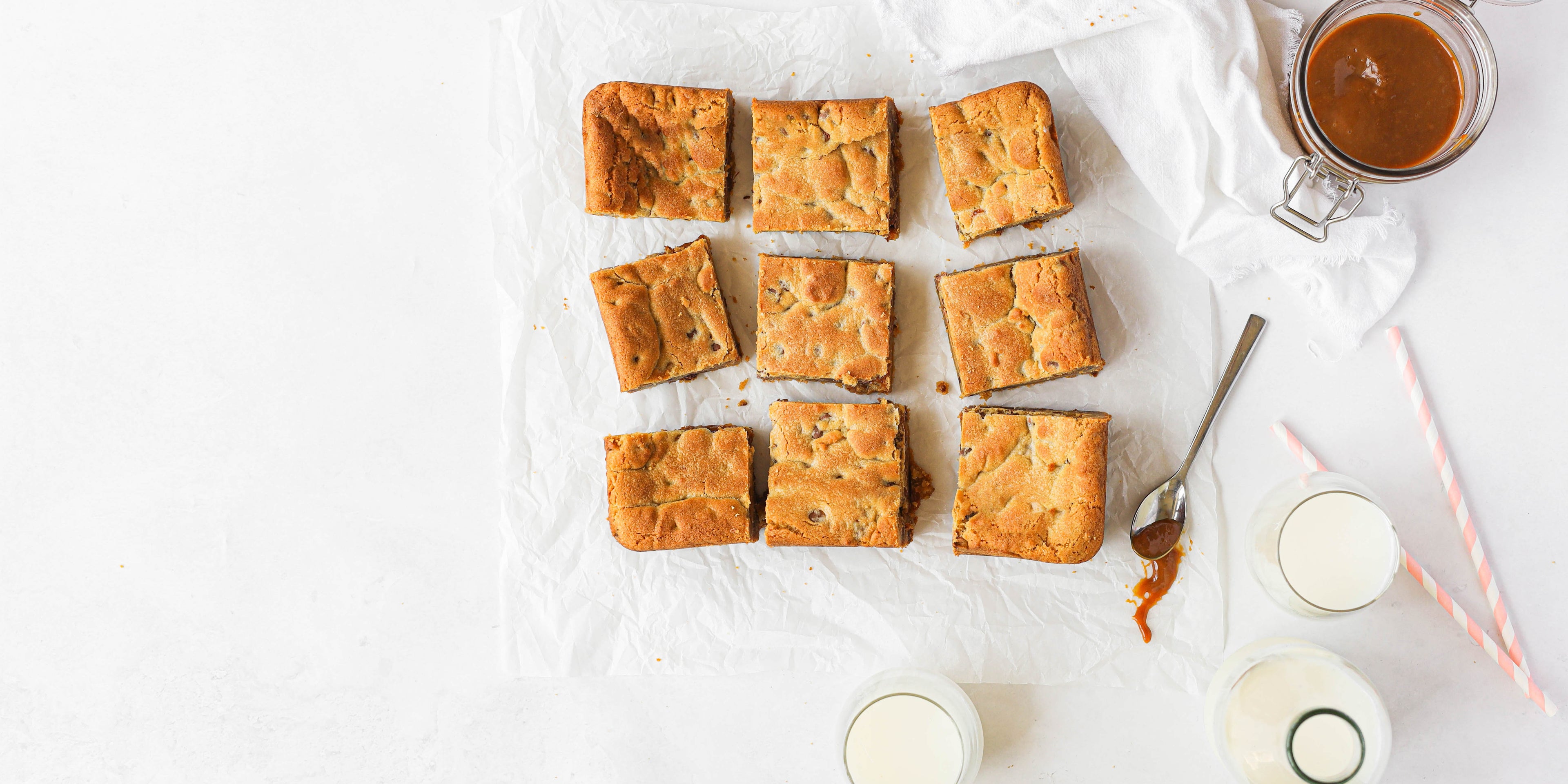 Salted Caramel Cookie Traybake on baking paper, with glasses of milk and straws