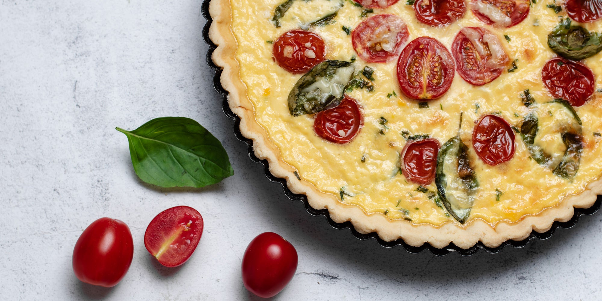 Close up of a Cheese & Tomato Quiche with chopped tomatoes and a basil leaf