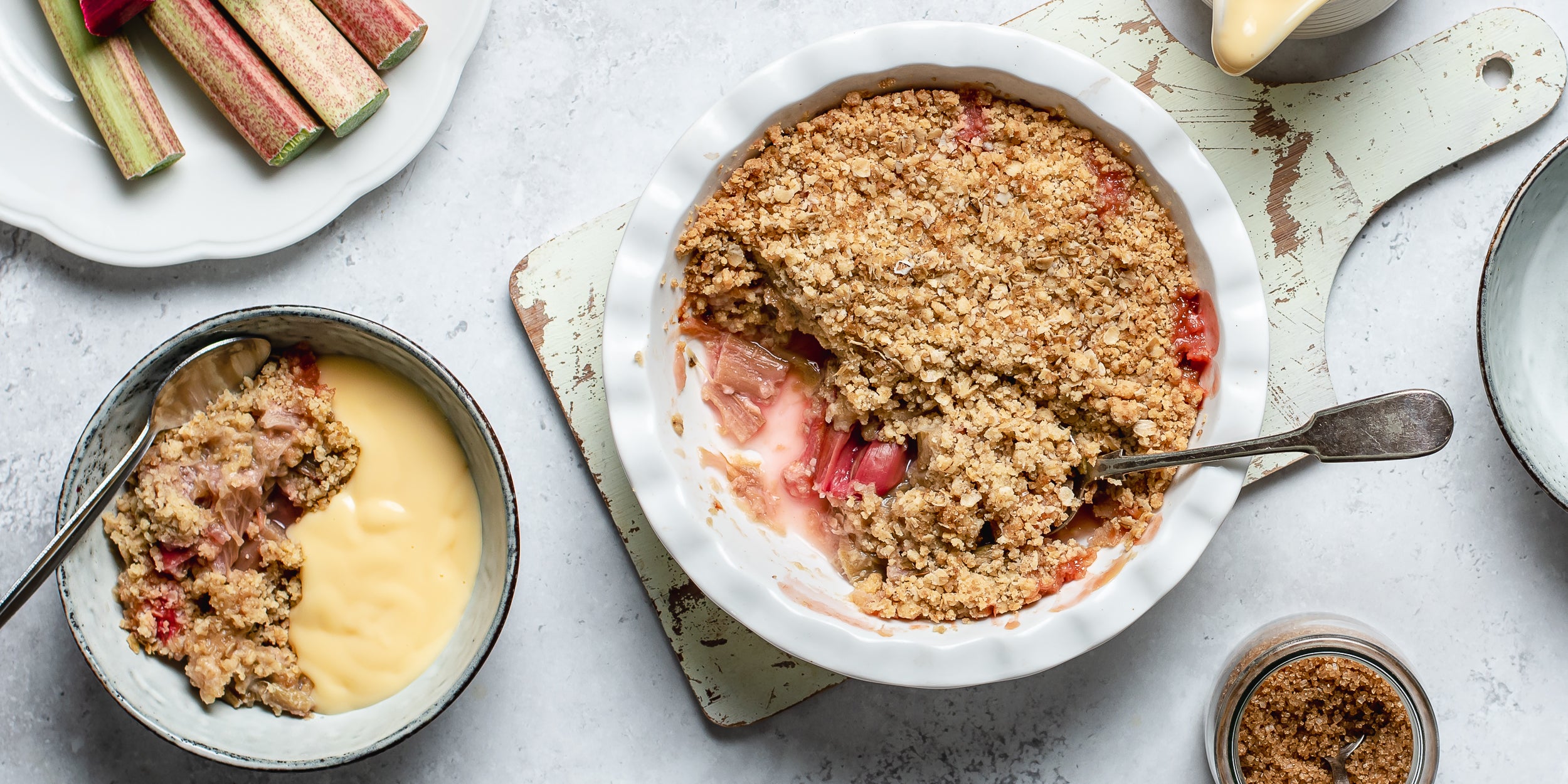 Top view of Rhubarb Crumble with a spoon serving up a portion, topped with vanilla custard