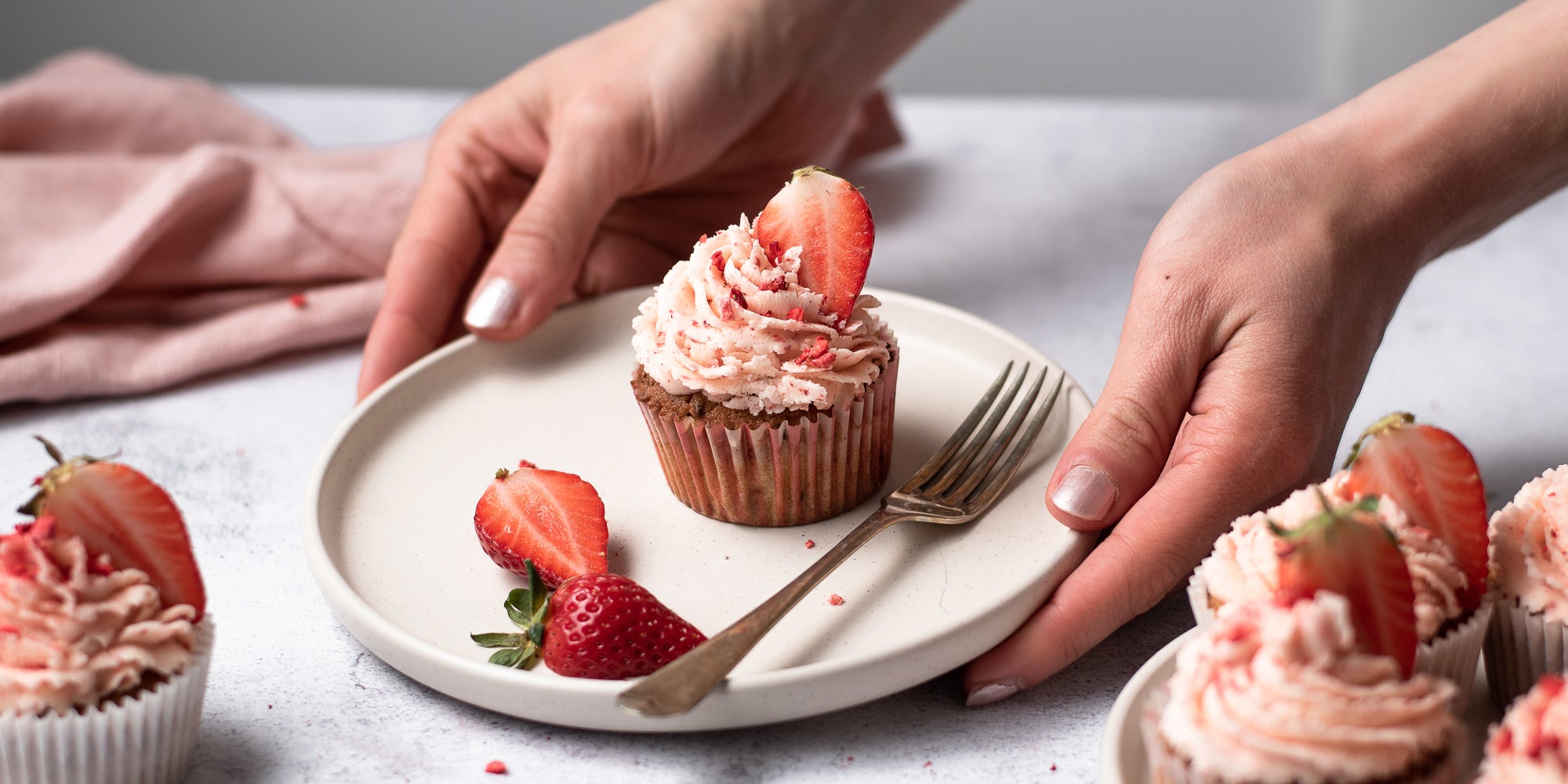 Person holding a plate of a strawberry cupcake topped with a strawberry