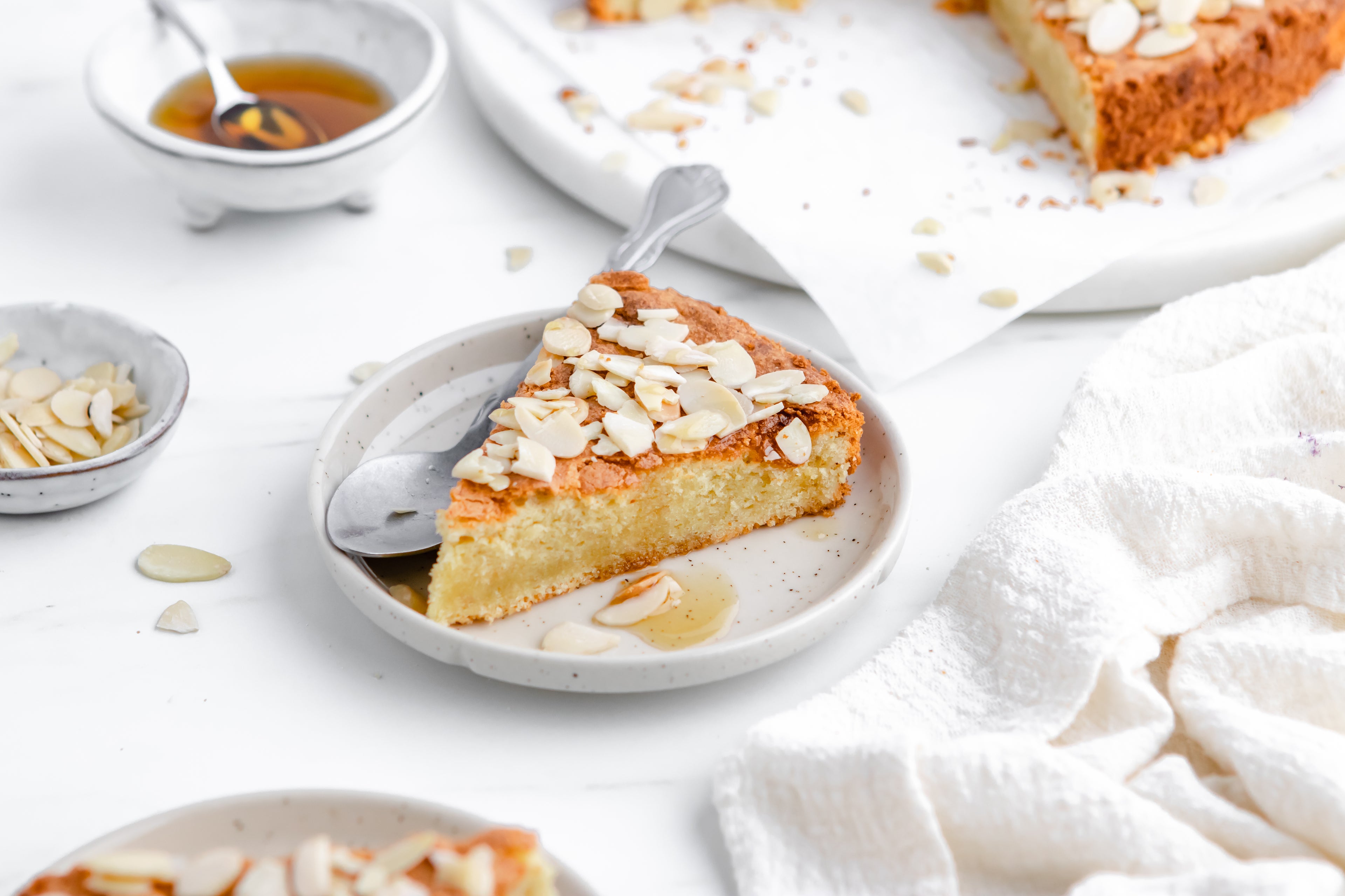 A slice of almond cake on a plate with a spoon