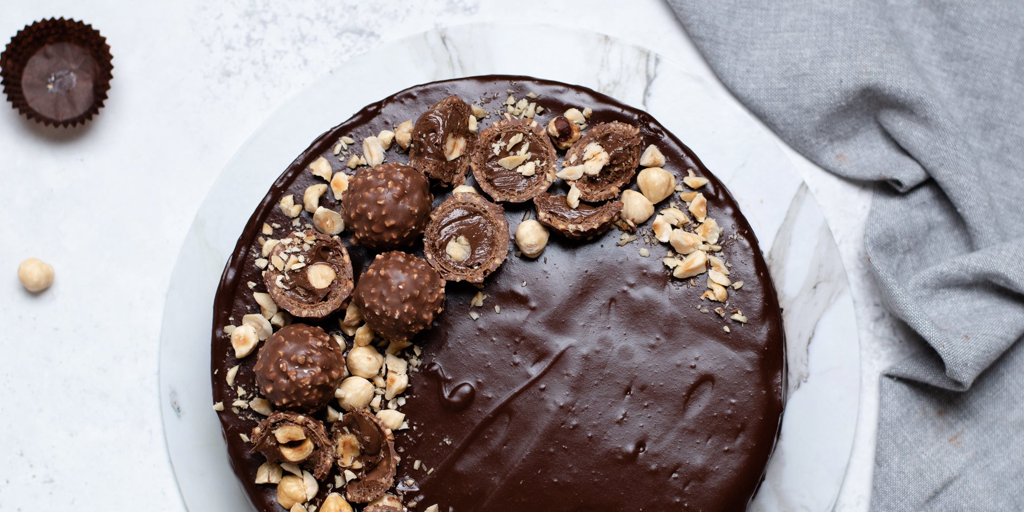 Top view of Gluten Free Chocolate Truffle Sachertorte, smothered in chocolate icing, decorated with Ferrero Rocher's and chopped hazelnuts on a marble serving plate