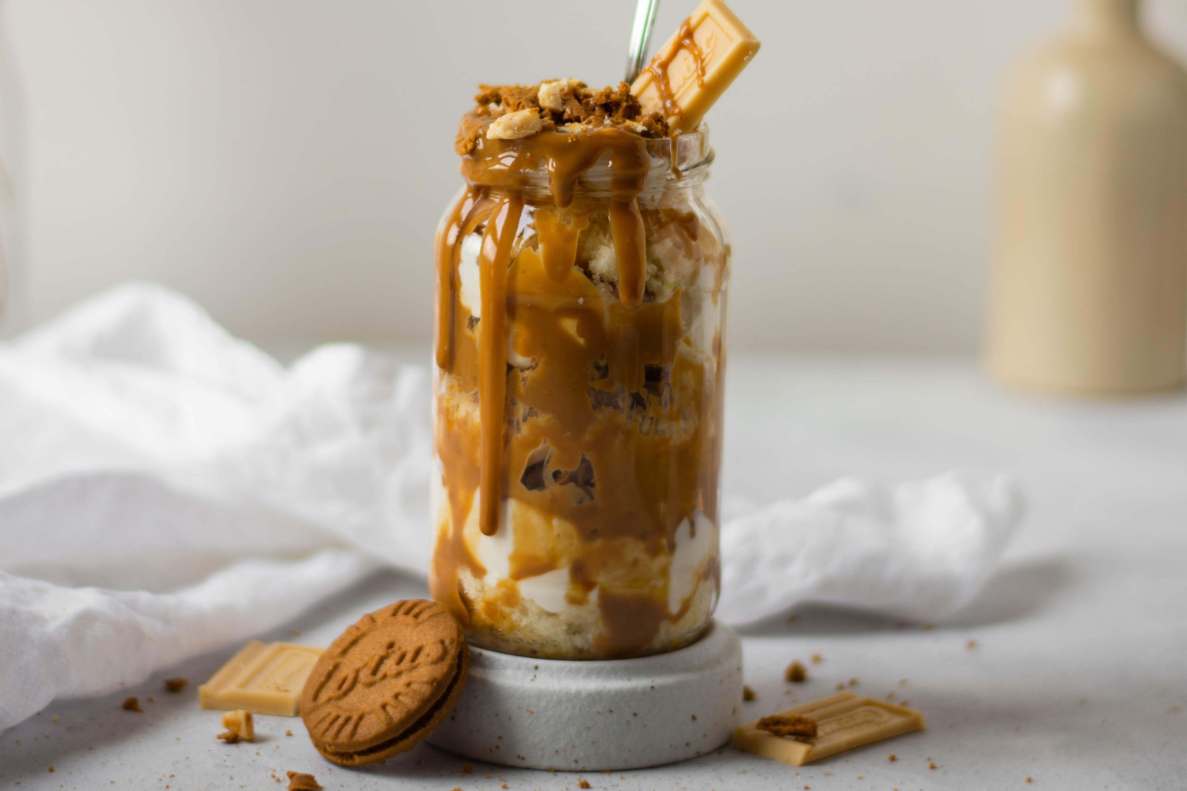 Biscoff & Caramac Cake Jar with biscoff dripping down the side of the jar, next to a Lotus biscuit and Caramac chocolate on the top