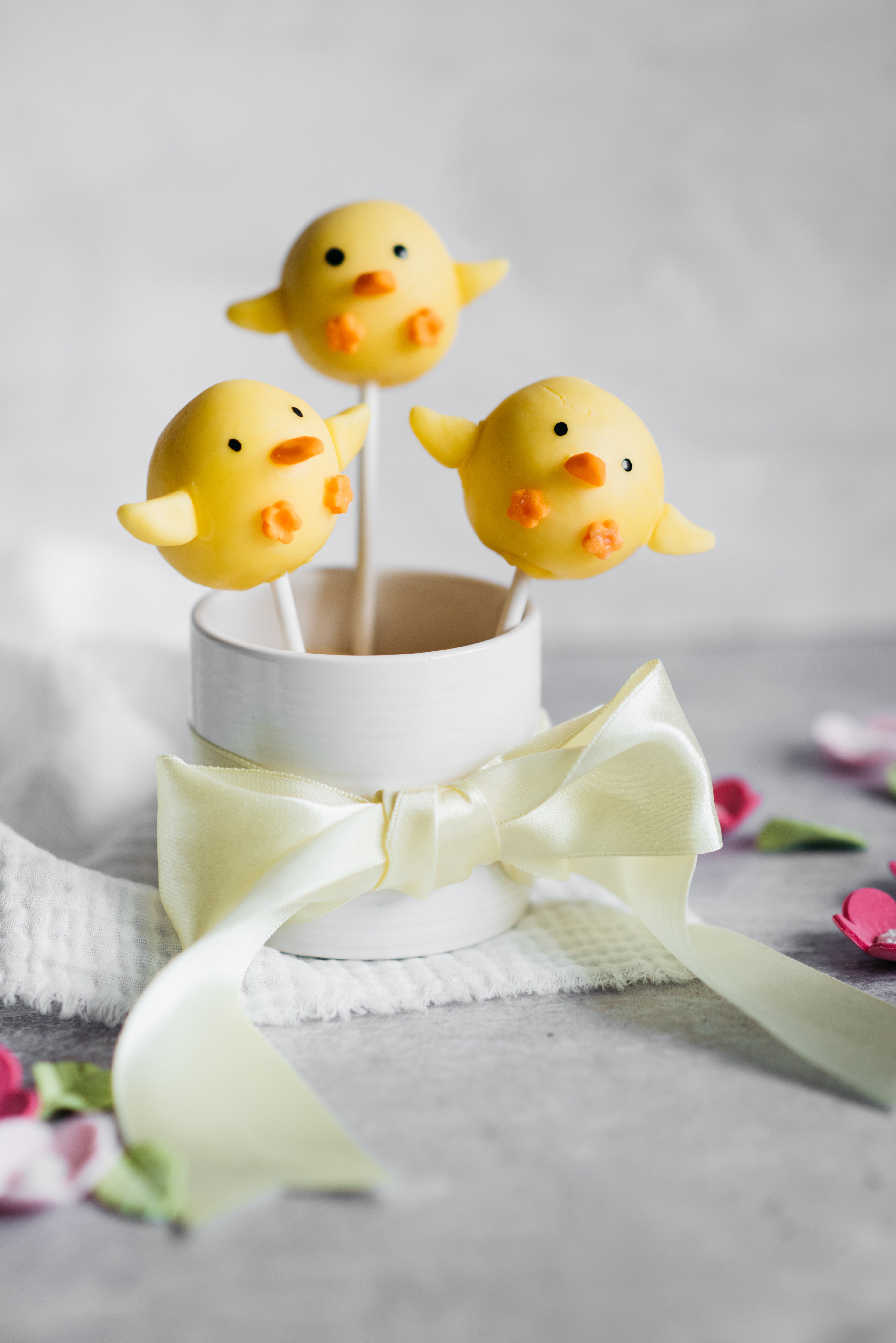 three chick cake pops covered in yellow chocolate in a mug wrapped in a bow