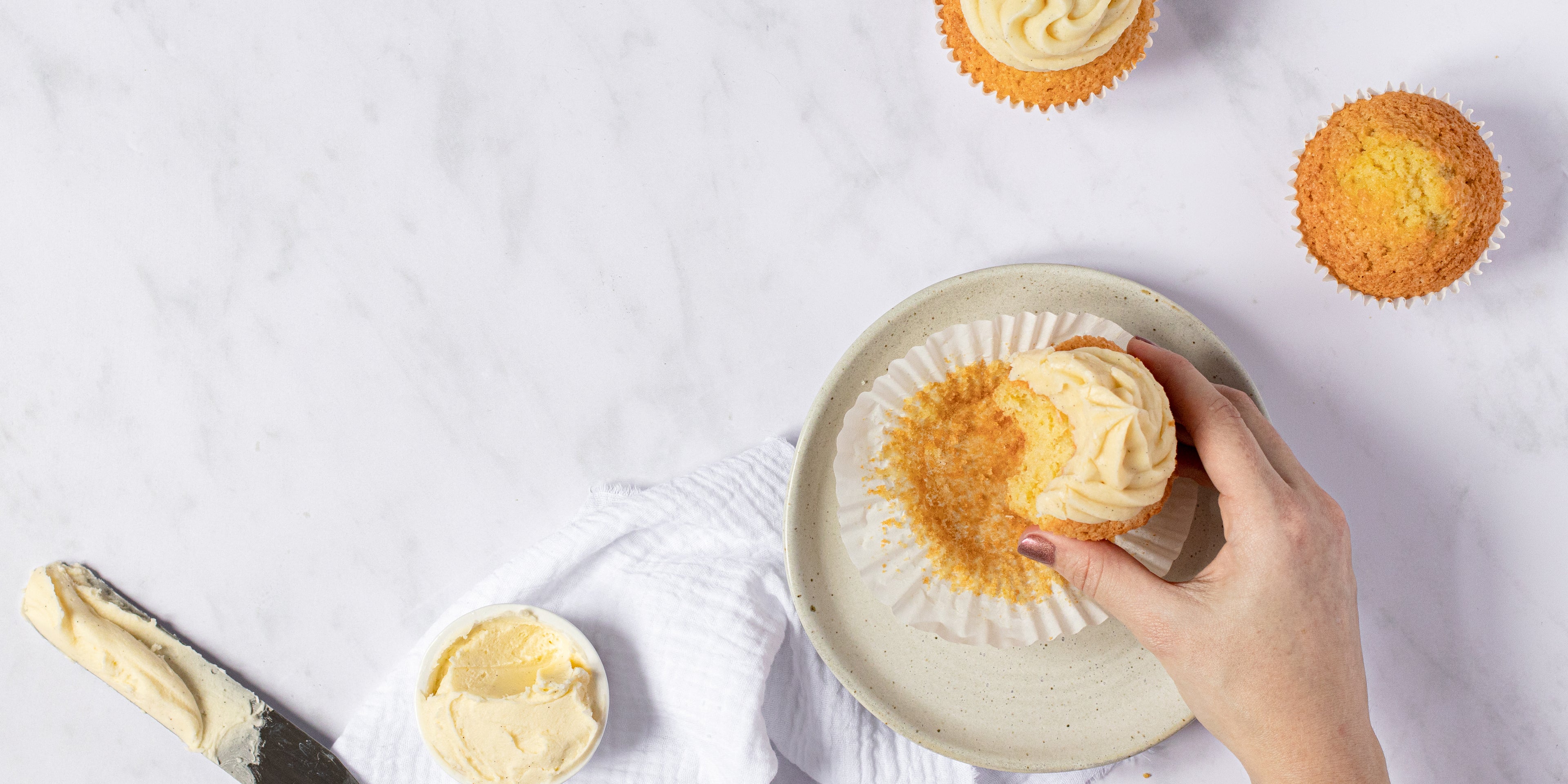 Hand holding a vanilla cupcake topped with vanilla buttercream bitten into