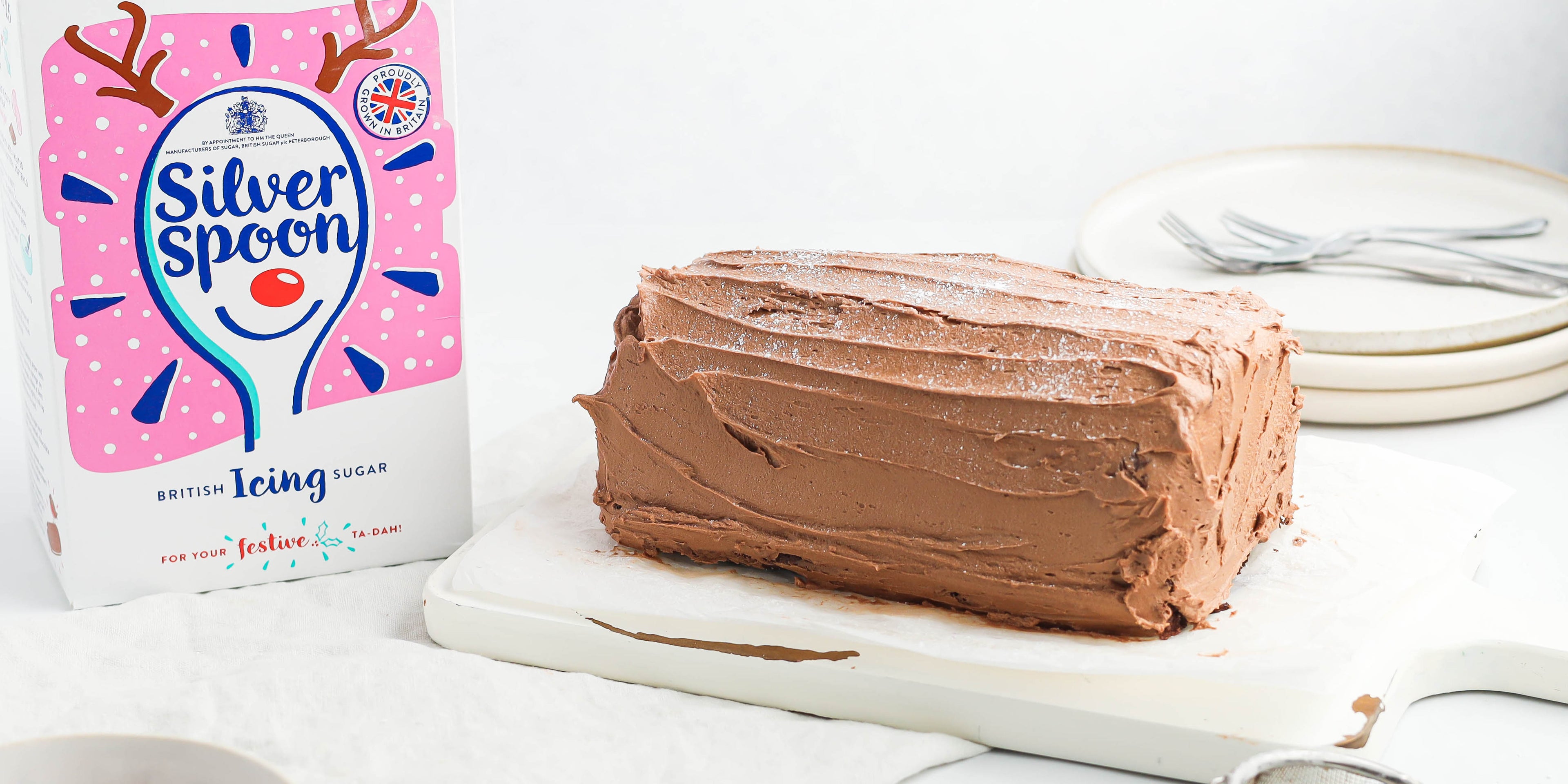 Chocolate Yule Log covered in rich chocolate icing next to a box of Silver Spoon icing sugar