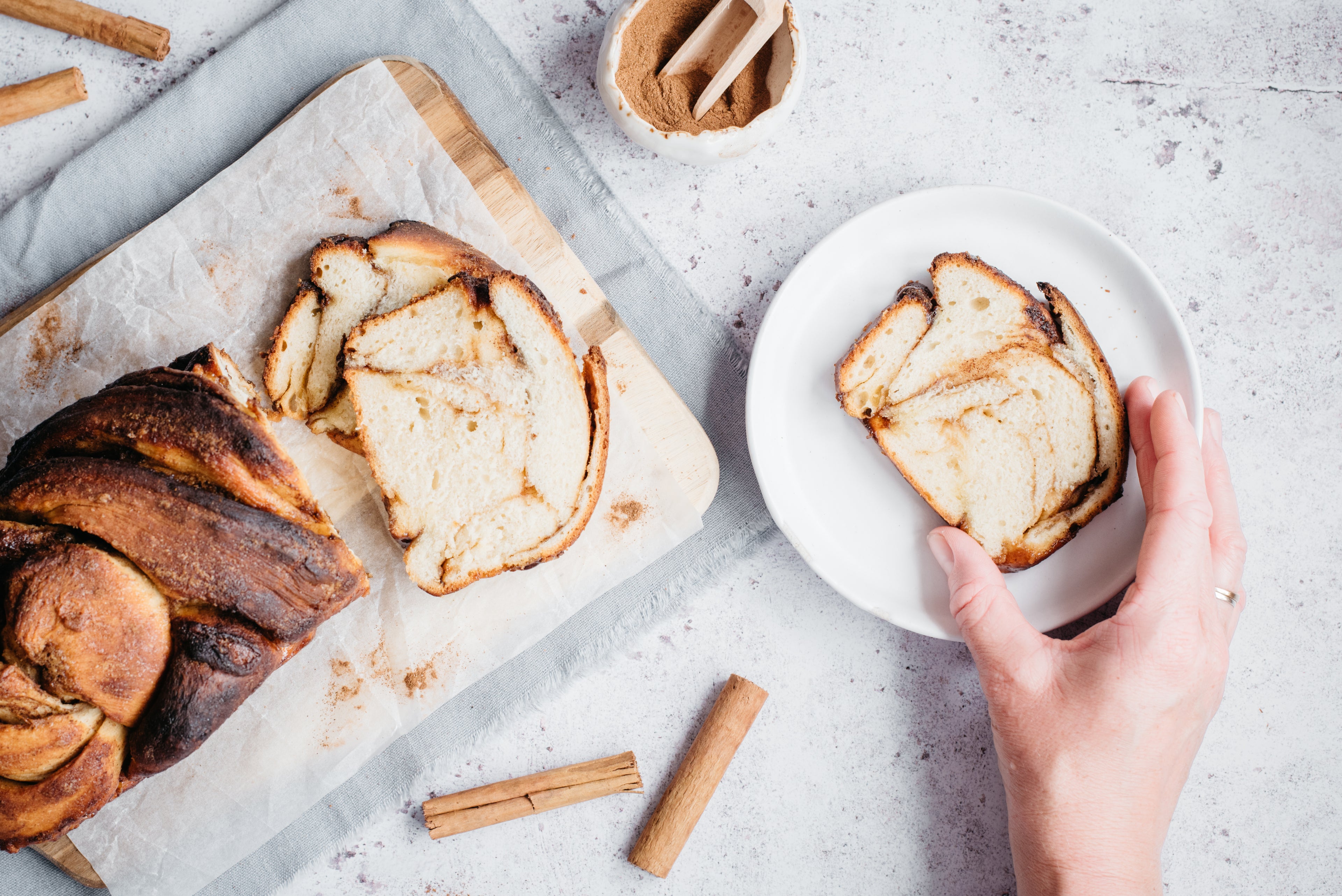 Cinnamon babka sliced on baking paper with cinnamon sticks and hand