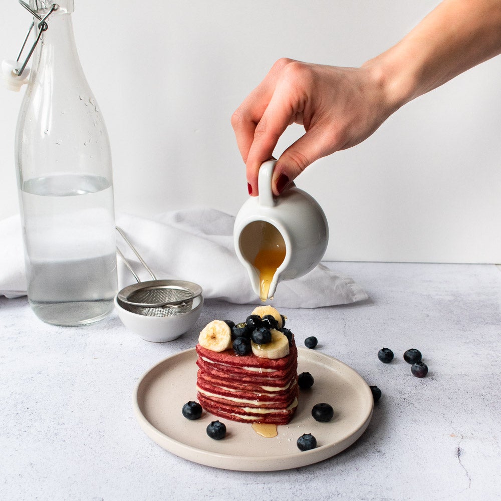 Syrup being poured over red velvet pancakes