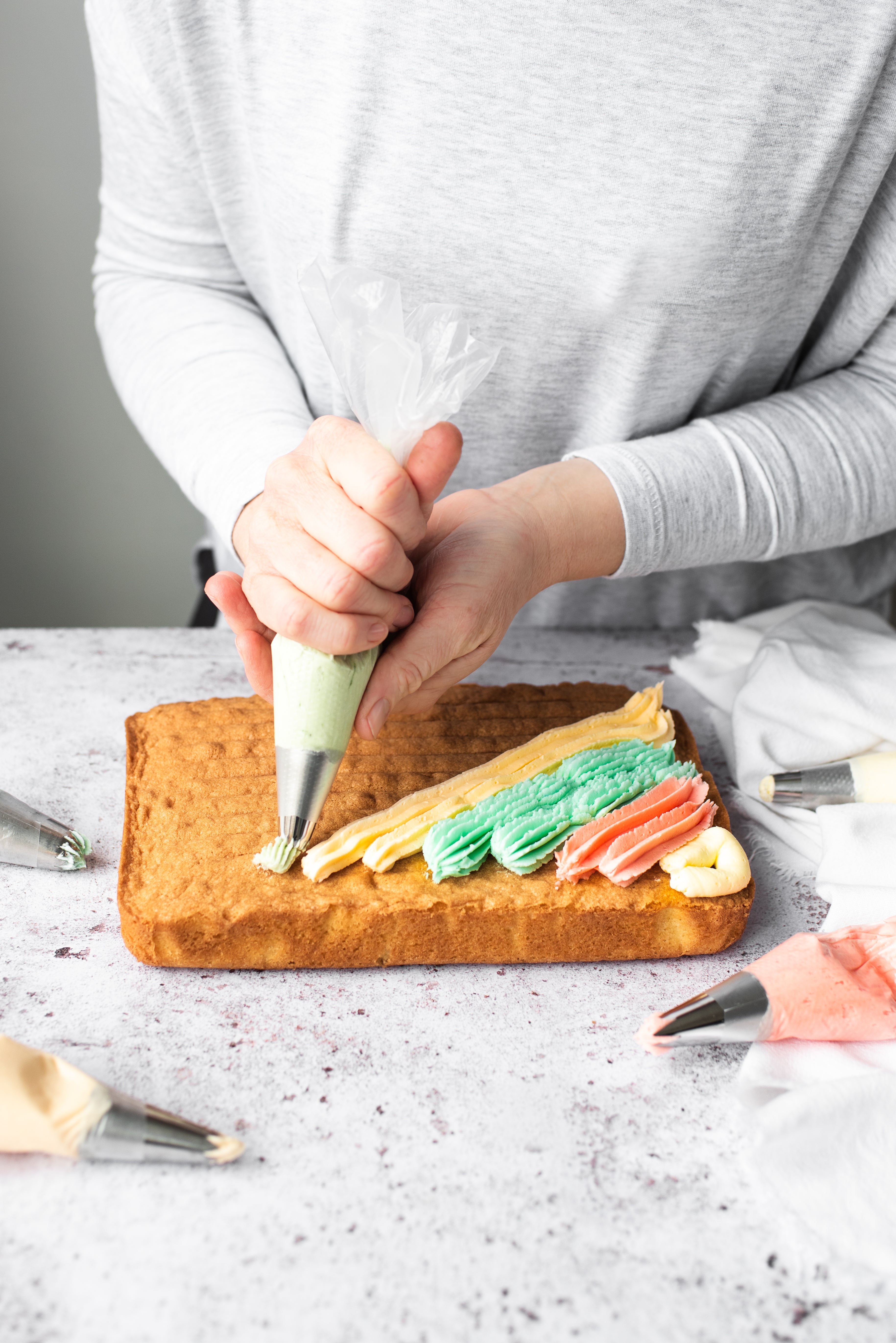 rainbow buttercream being piped onto a traybake cake