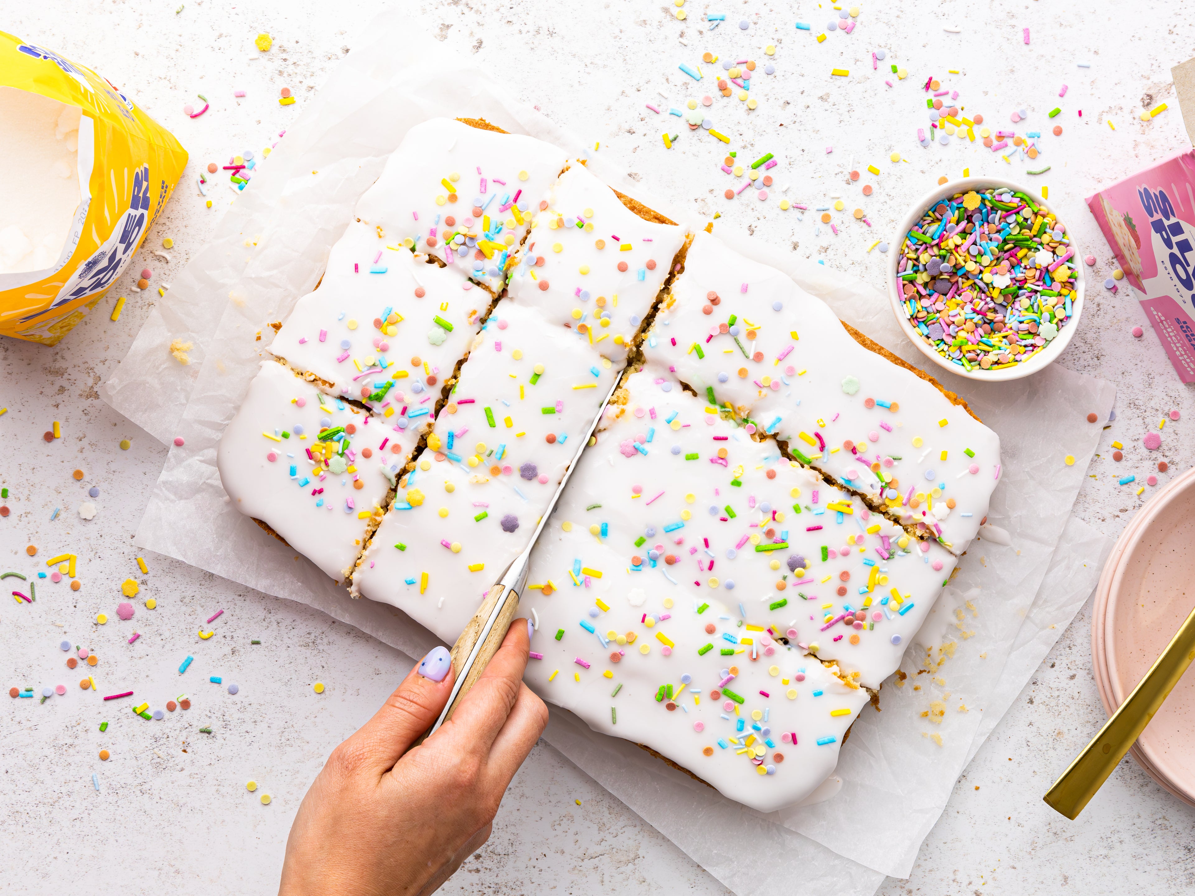 Cake topped with icing and sprinkles being chopped into squares