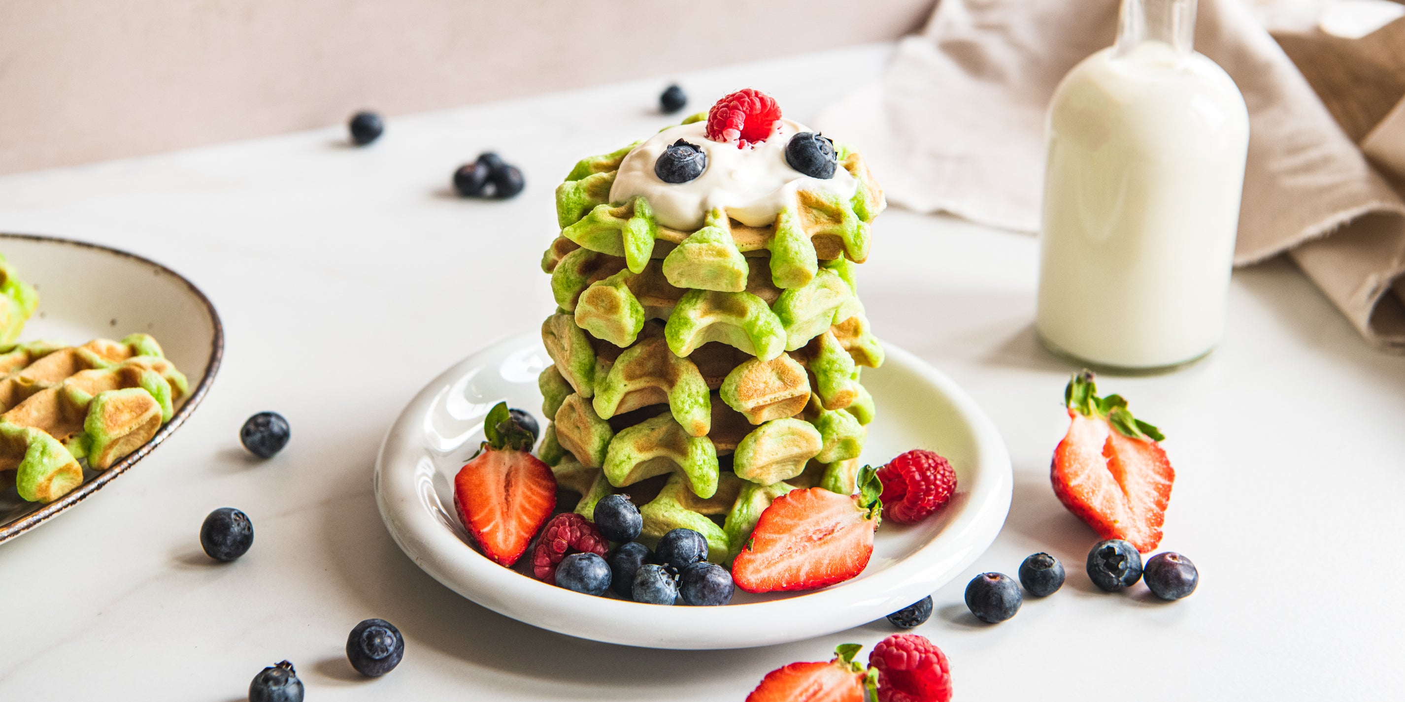 Close up of a fresh stack of Pandan Waffles, drizzled with fresh berries and a dollop of yoghurt