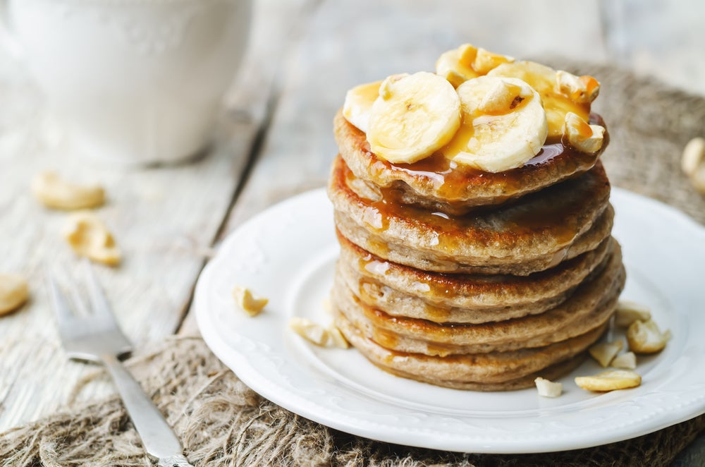 Stack of vegan gluten free pancakes topped with sliced banana and syrup