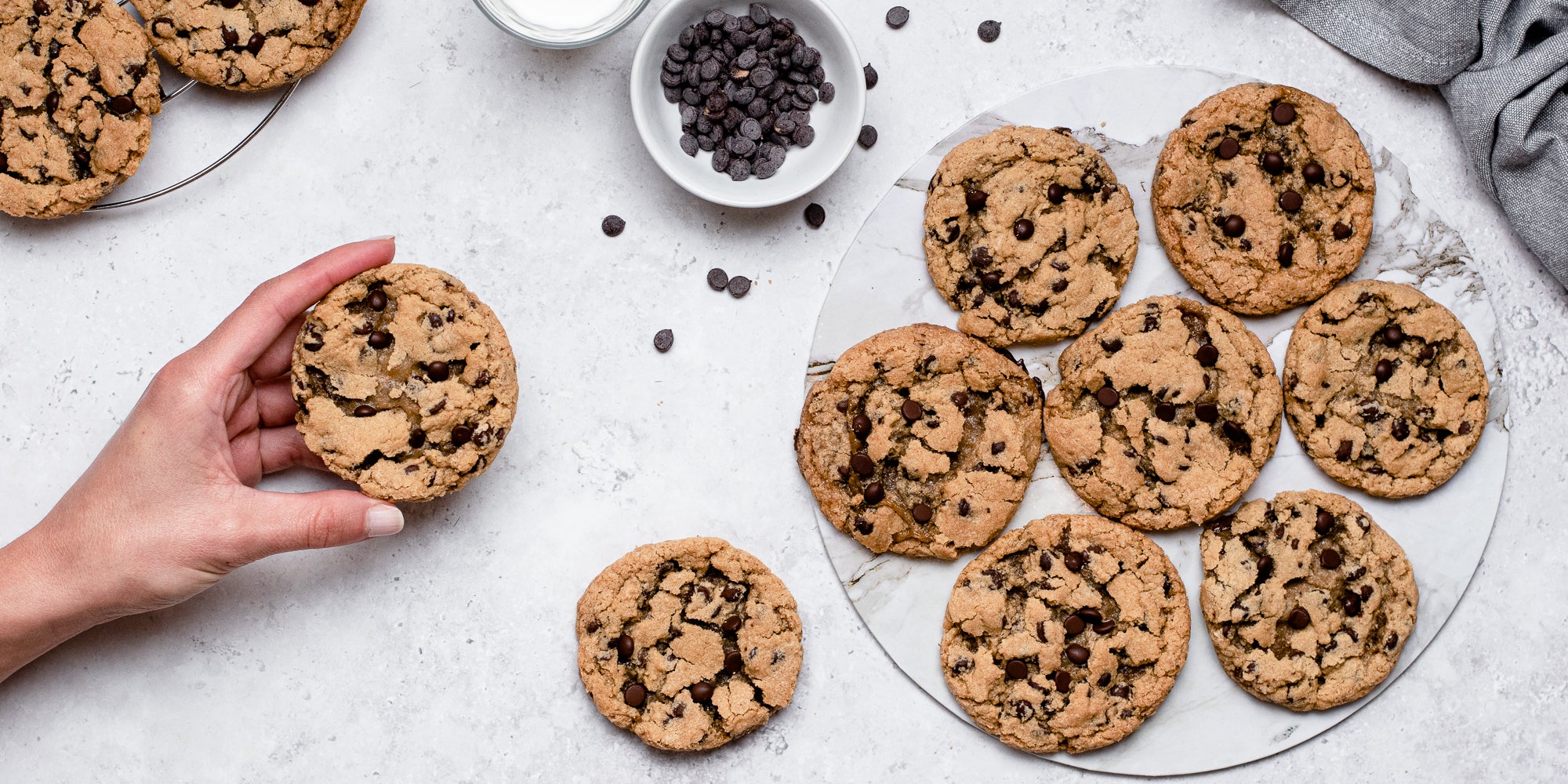 Top down view of a hand holding a vegan and gluten free chocolate chip cookie next to a plate of cookies