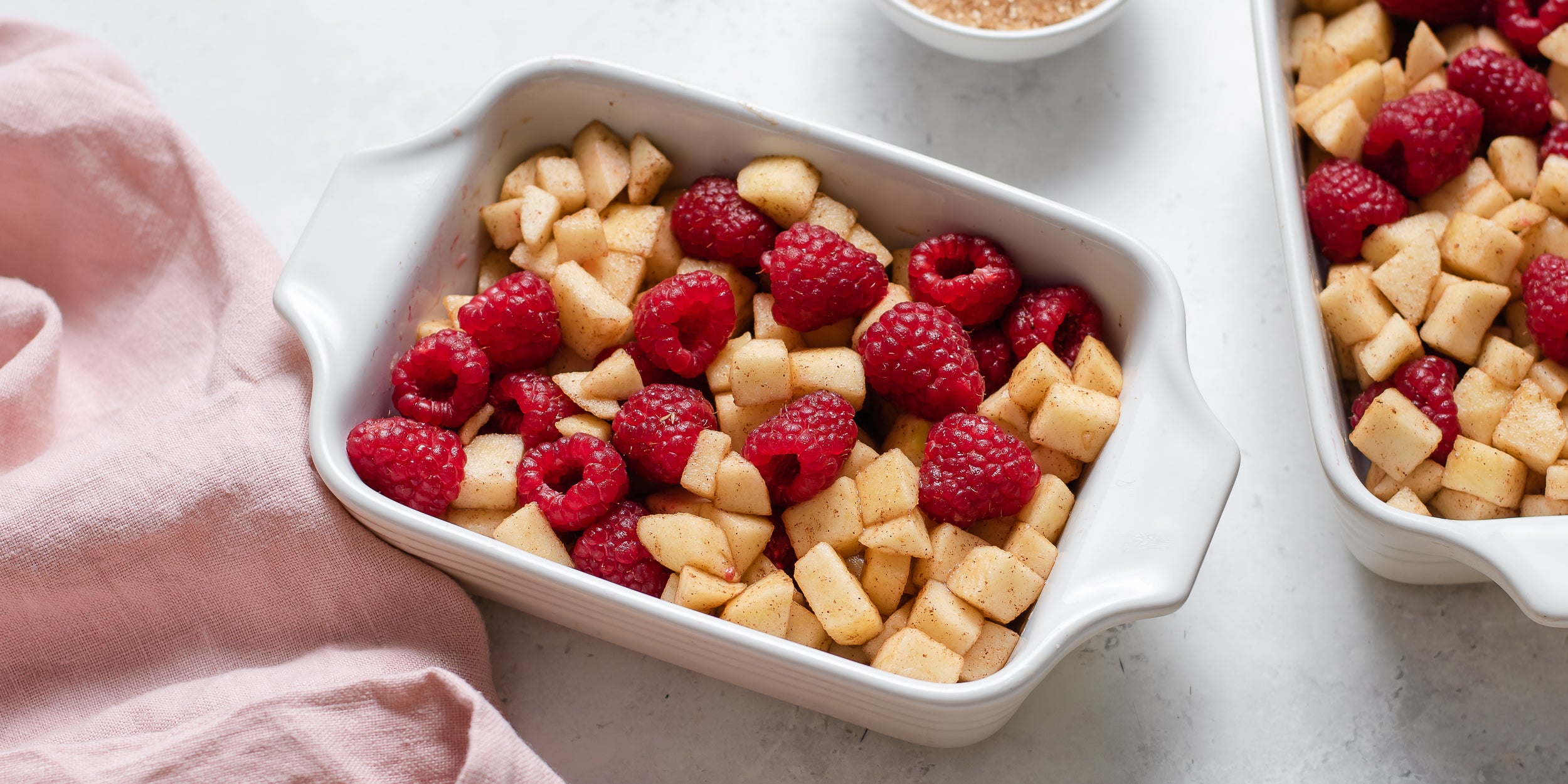 Chopped apple and fresh raspberries in a baking dish ready to top with crumble topping before baking in the oven