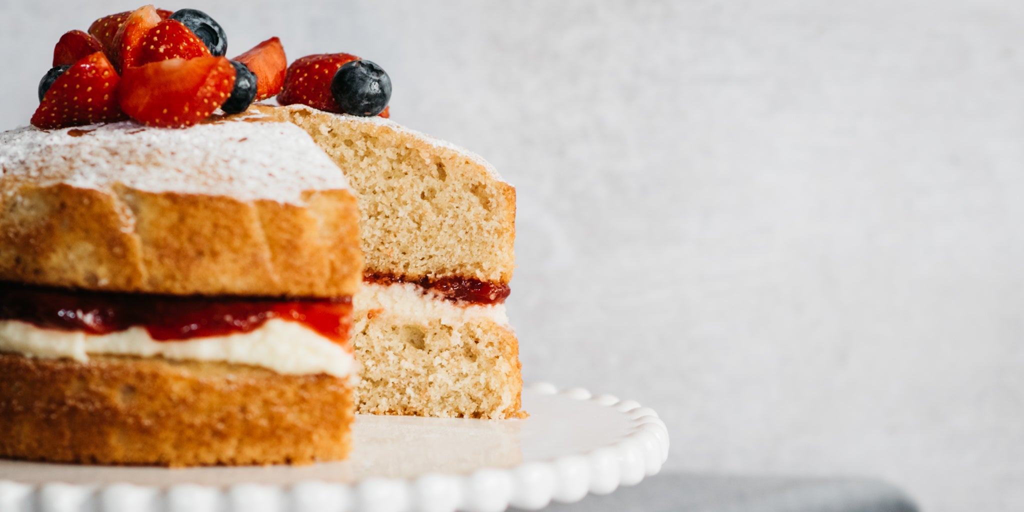 Close up of a Wholemeal Victoria Sponge with a slice cut out of it showing the moist inside filled with cream and jam