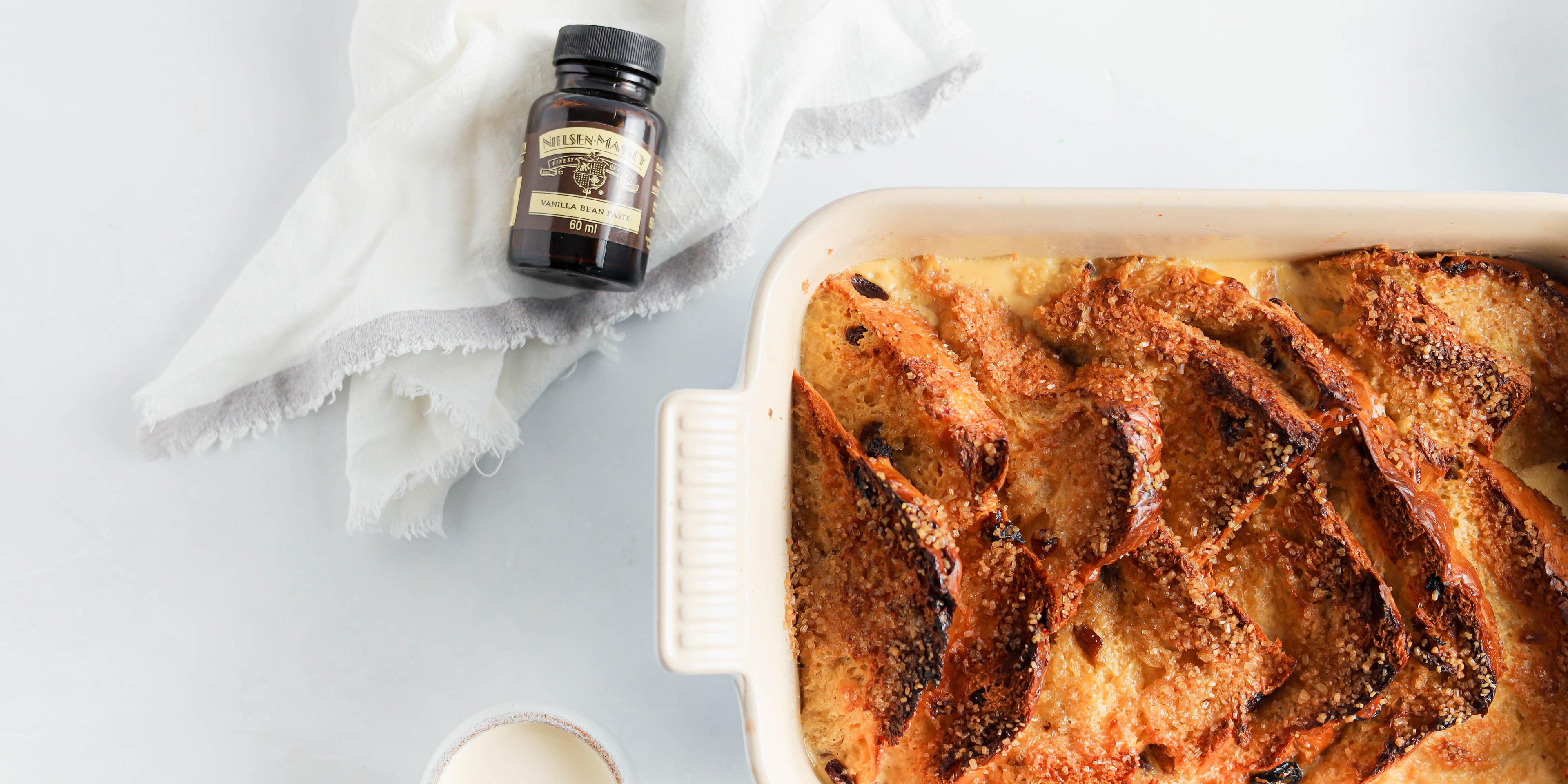 Close up of Panettone Bread & Butter Pudding next to a small bottle of Nielsen-Massey Vanilla extract