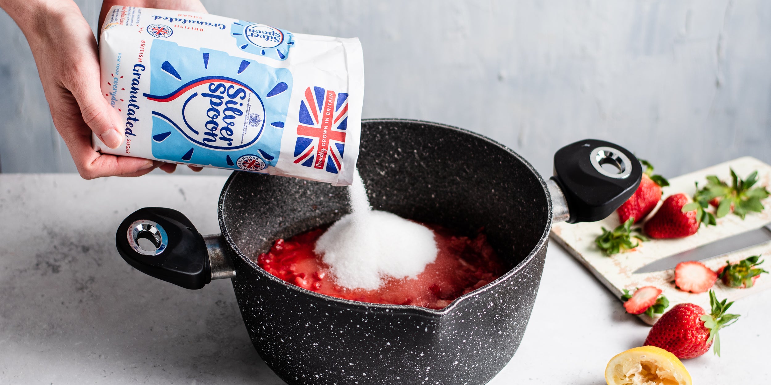Silver Spoon Granulated Sugar being poured into a hot pan of strawberries