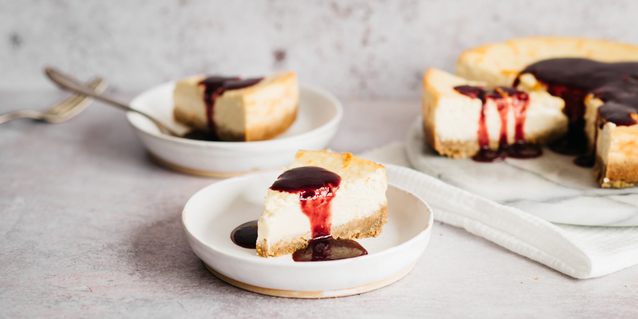 A slice of baked cheesecake in a bowl covered in raspberry sauce