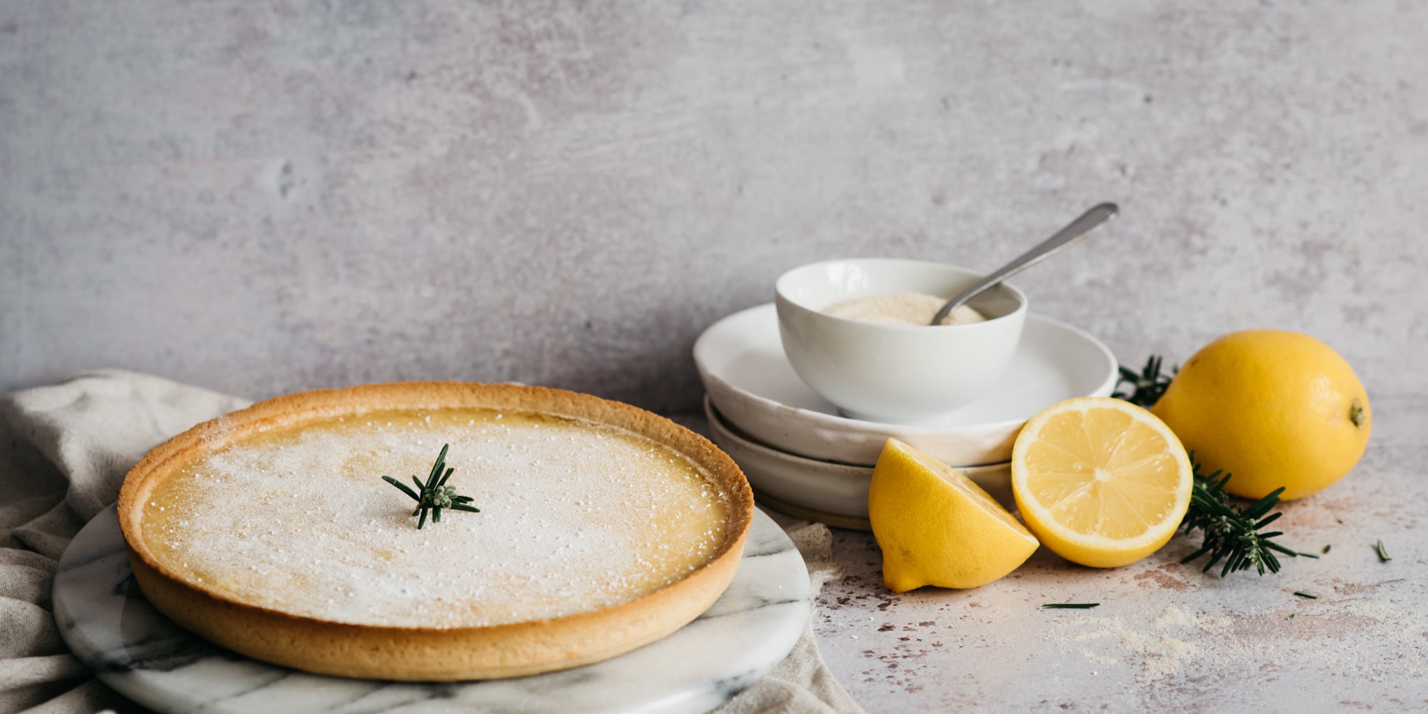 Baked Lemon Tart dusted with Silver Spoon Icing Sugar, next to sliced lemon 