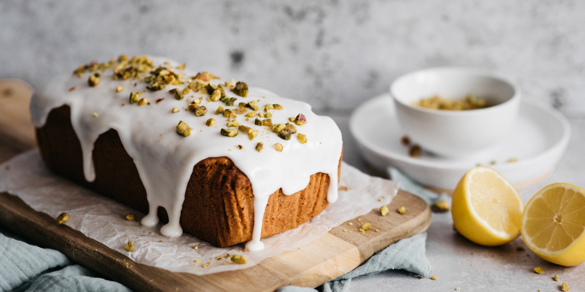 Close up of Gluten Free Vegan Lemon Drizzle Cake on a serving board ready to slice, topped with ground nuts