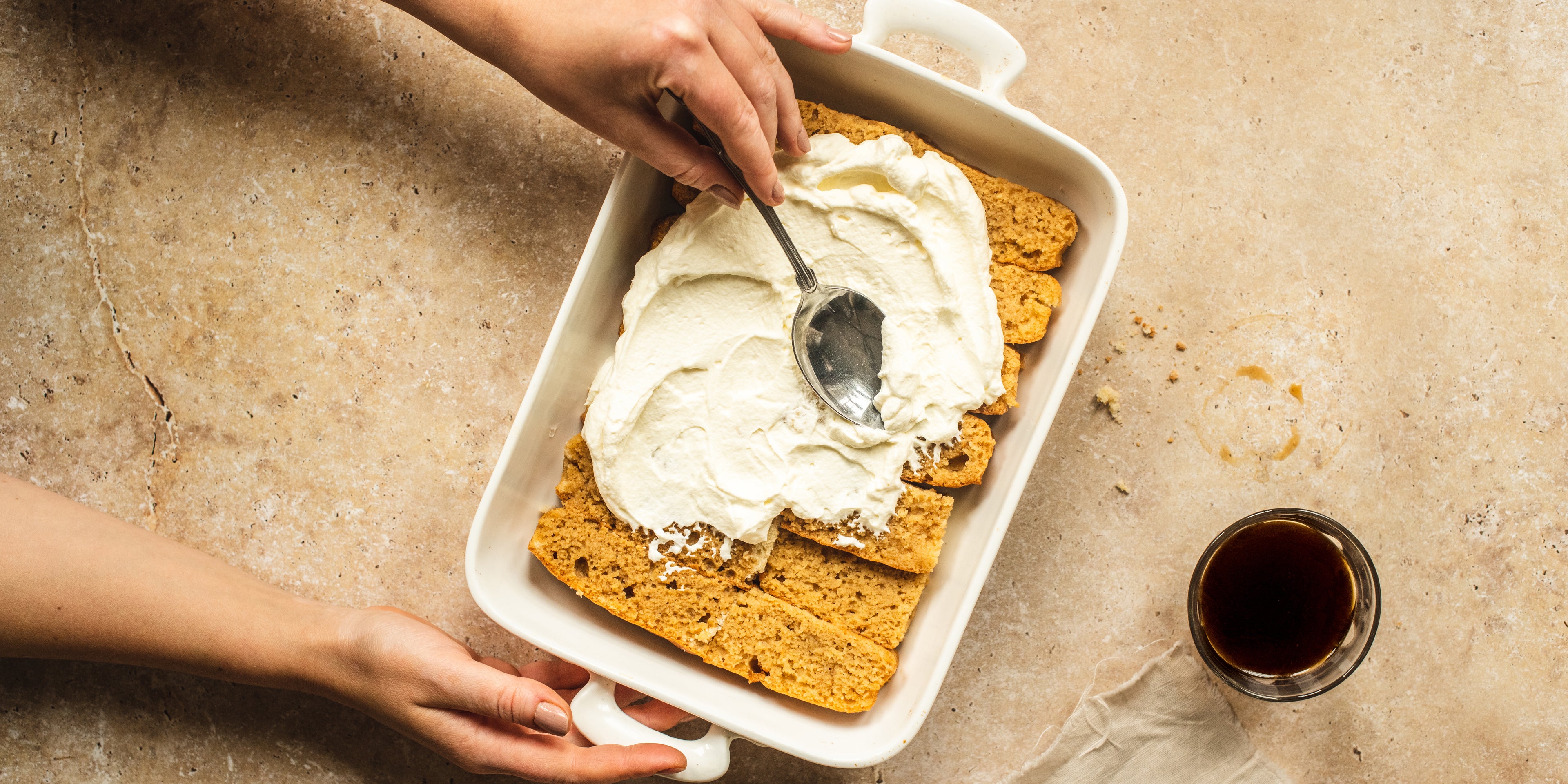 Top view of hands smoothing plant based cream over the coffee soaked layer of a Vegan Tiramisu