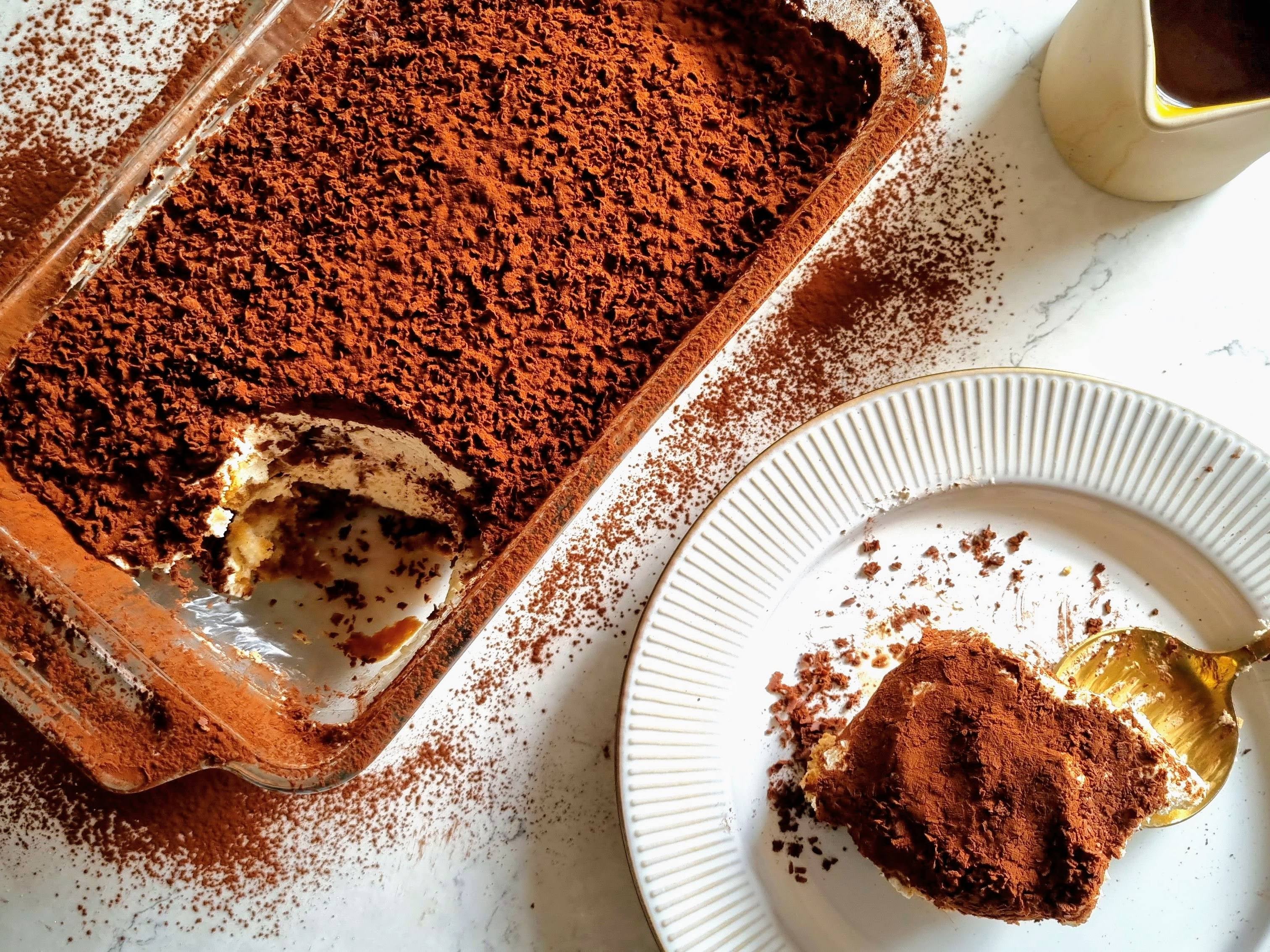 Slice being taken out of a homemade tiramisu and put onto a white plate