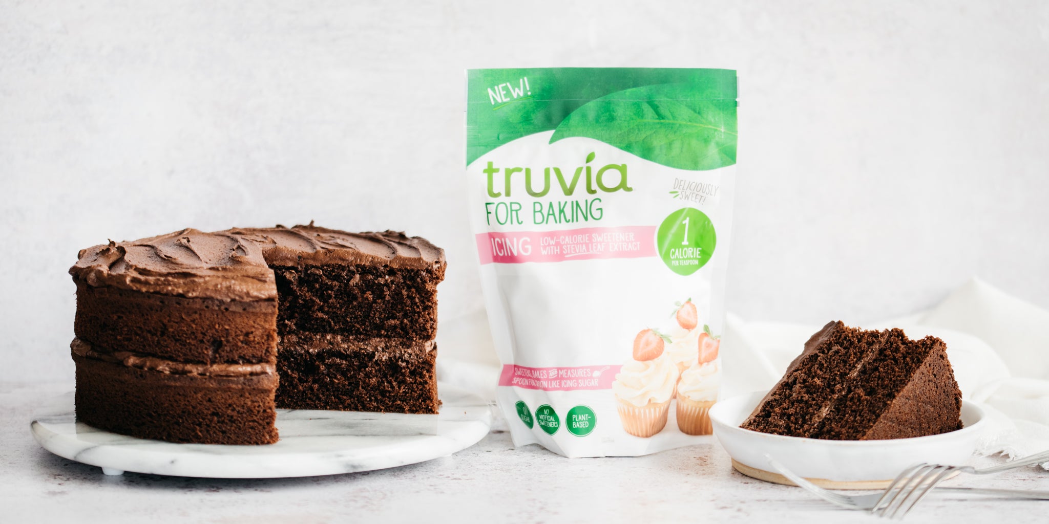 Chocolate Cake on a marble cake plate, pack of Truvia icing sugar and slice of chocolate cake beside it.