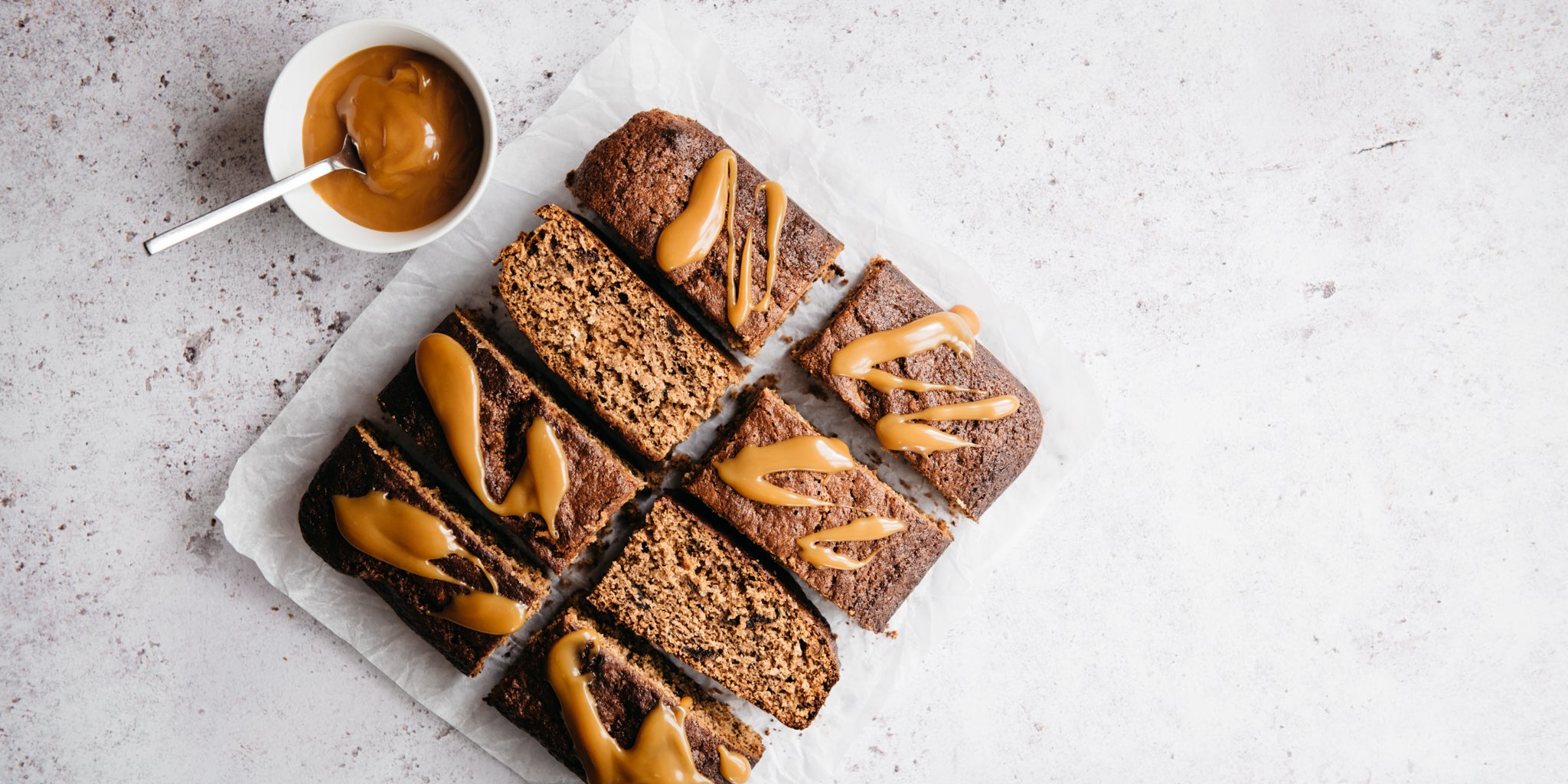 Ultimate Wholemeal Sticky Toffee Pudding top view, sliced into squares next to a bowl of sticky toffee sauce to drizzle