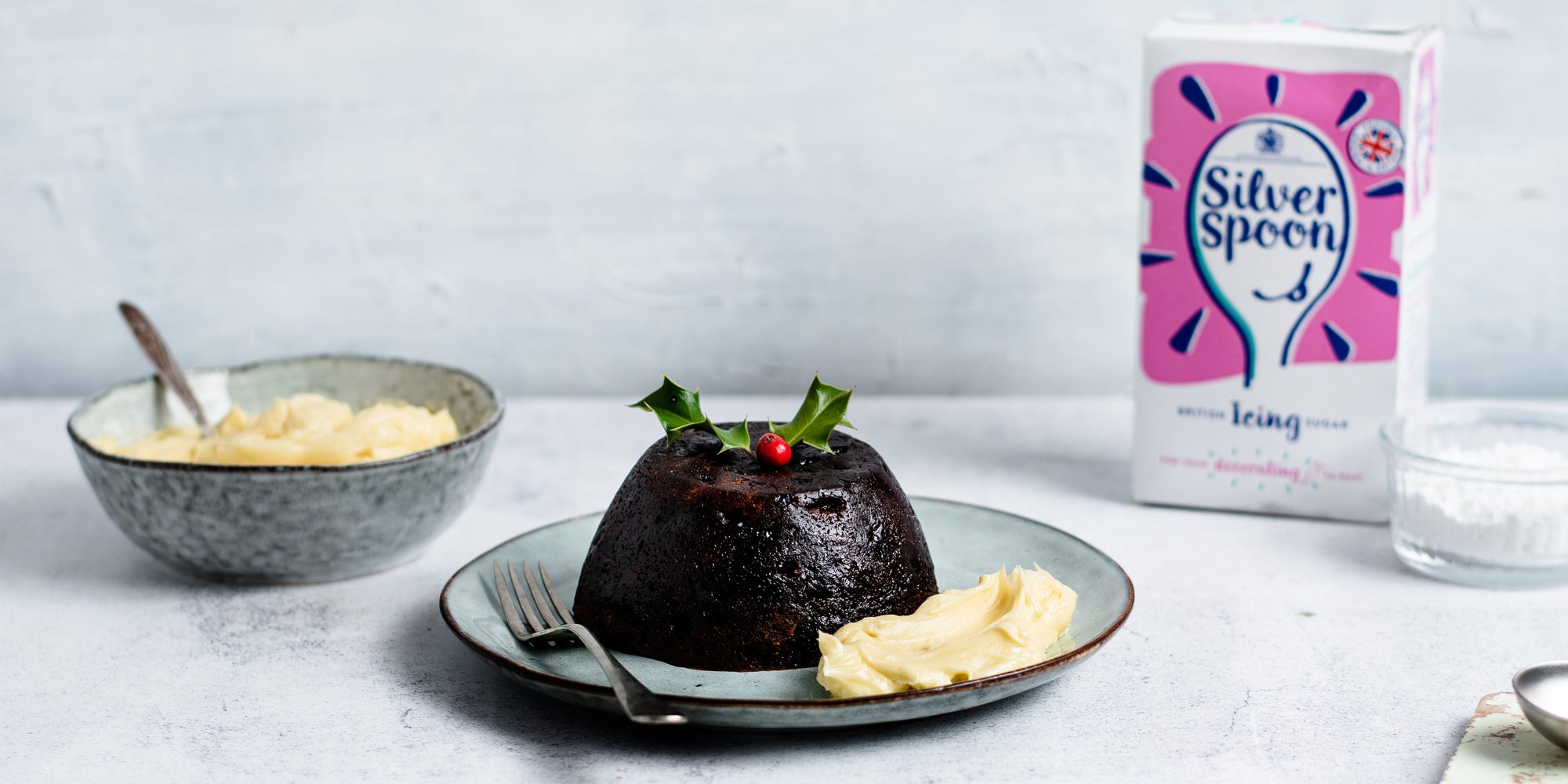 Close up of christmas pudding with a serving of Brandy butter, next to a box of Silver Spoon icing sugar 