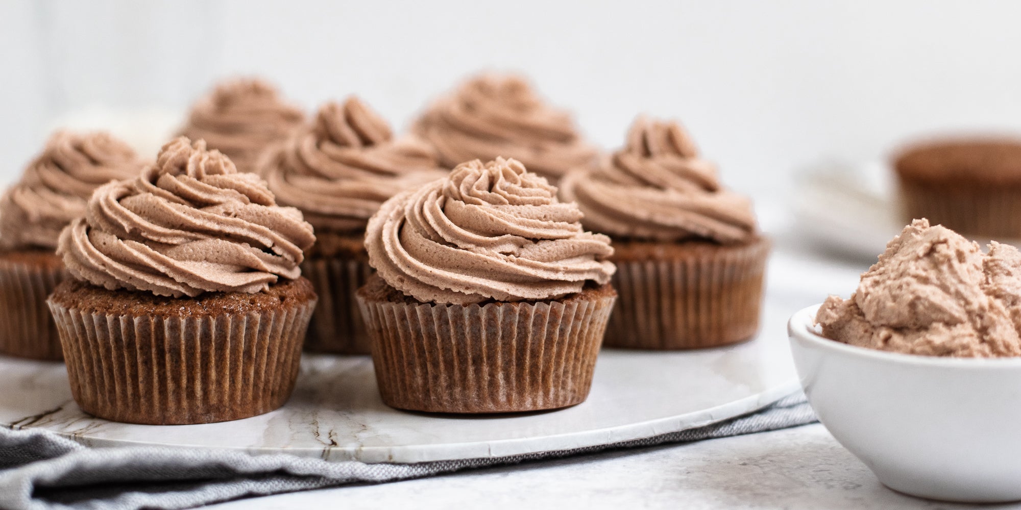 Close up of Dairy Free Vegan Chocolate Buttercream on top of cupcakes. Bowl of Dairy Free Vegan Chocolate Buttercream in the foreground