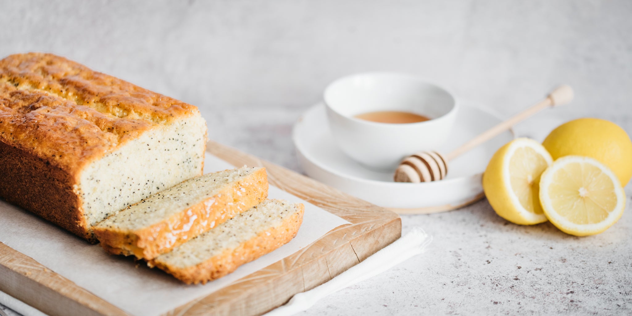 Lemon loaf on a chopping board with a bowl of honey beside and some chopped lemons