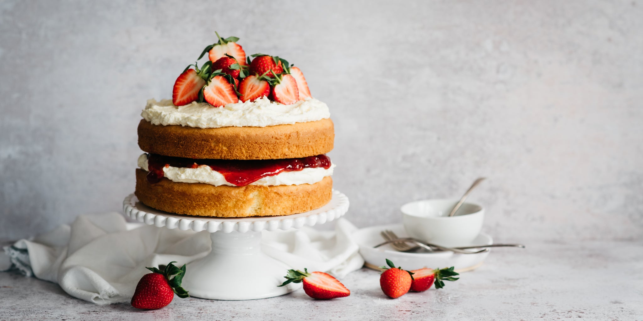 Gluten Free Victoria Sponge served on a cake stand, topped with sliced strawberries