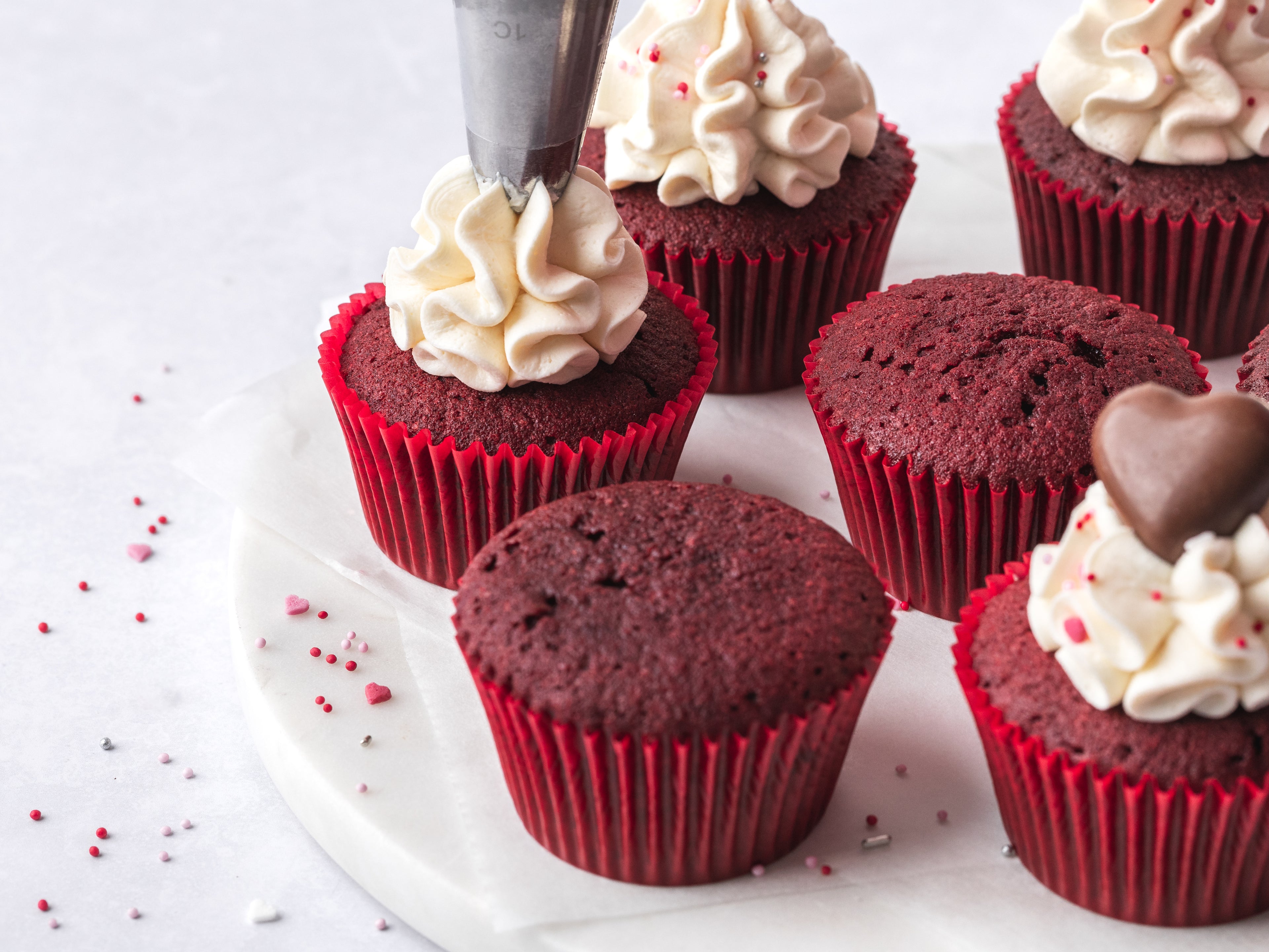 Piping nozzle piping buttercream on top of red velvet cupcakes