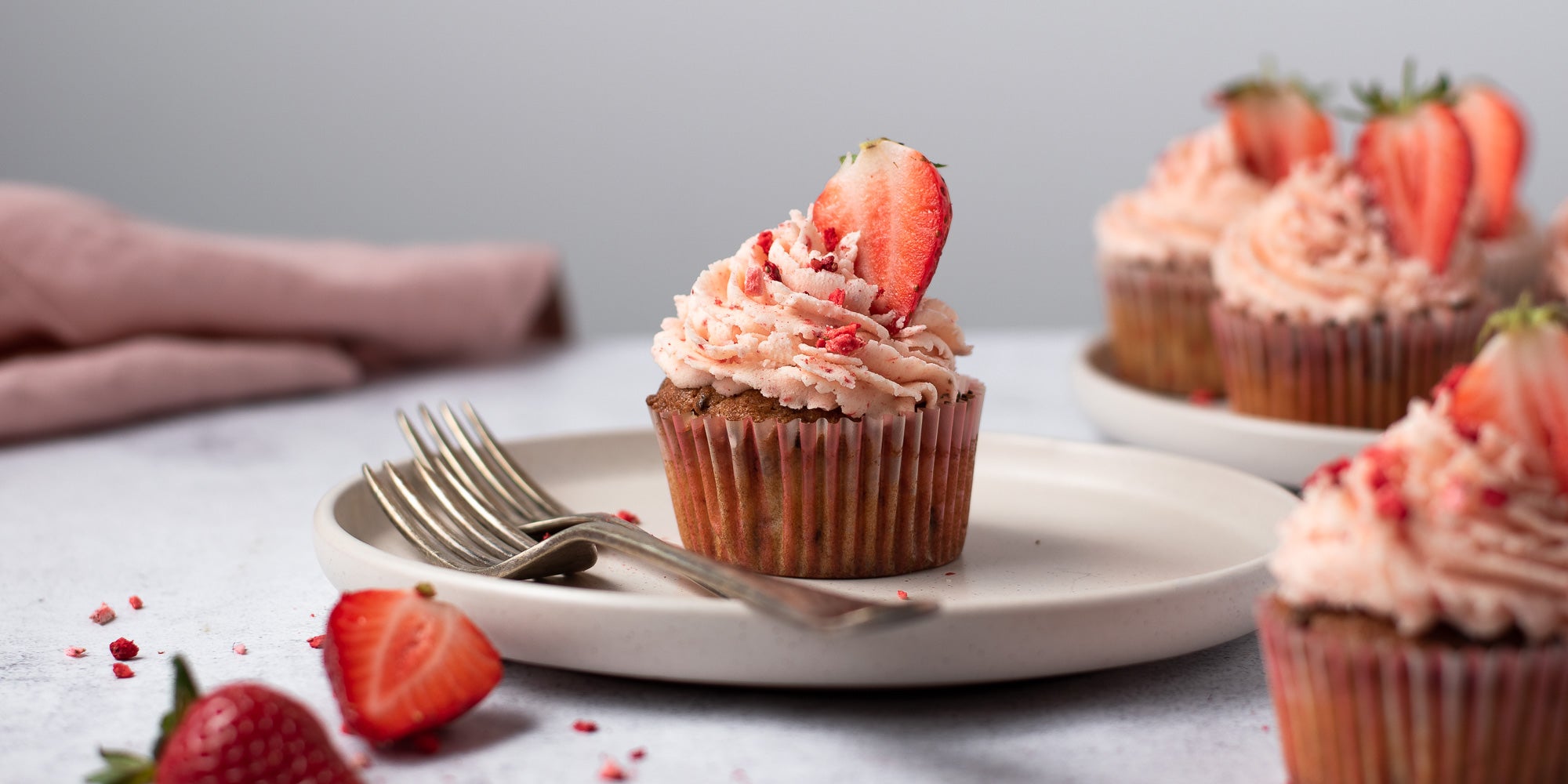 Strawberry cupcakes topped with strawberry buttercream on a plate next to a fork