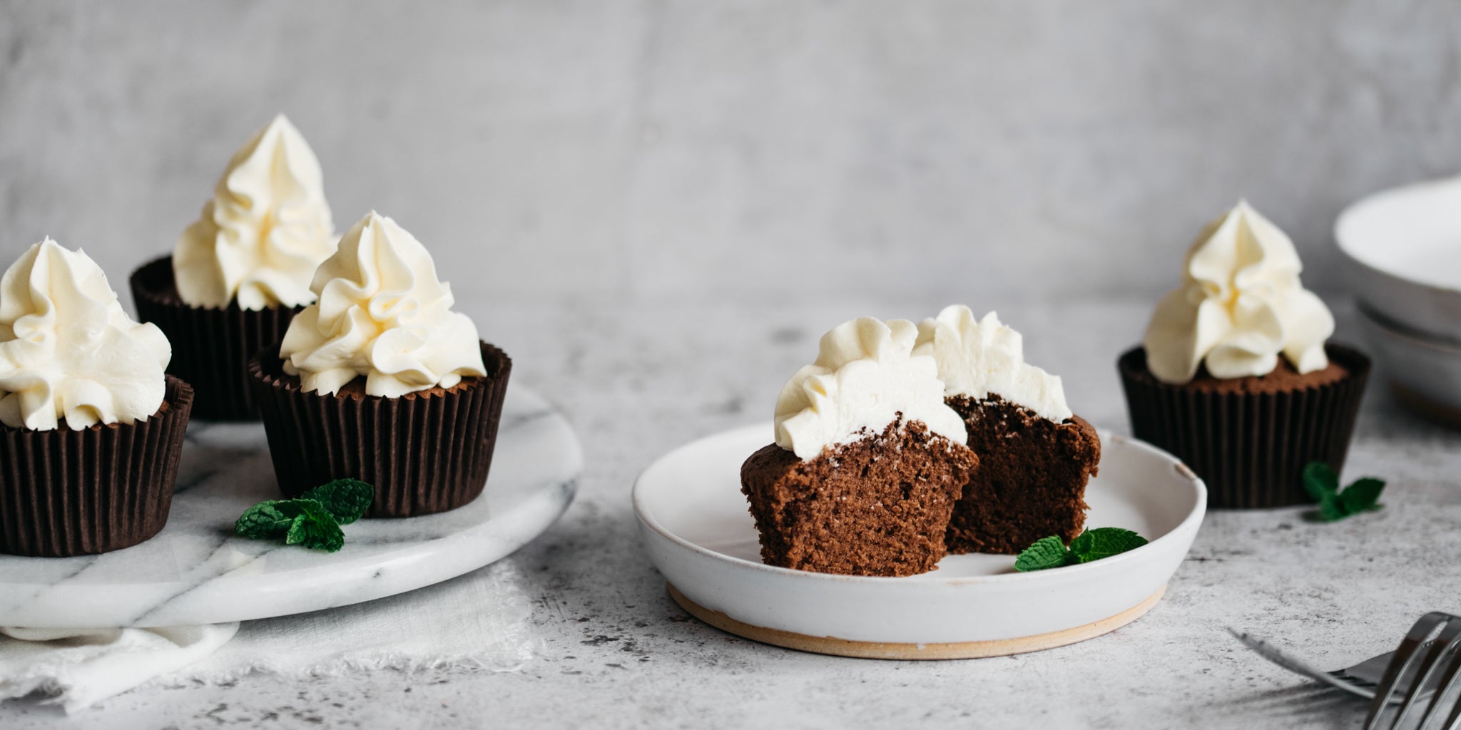 Chocolate & Peppermint Cupcakes served on a marble cake stand, with a cupcake sliced in half showing the fluffy insides