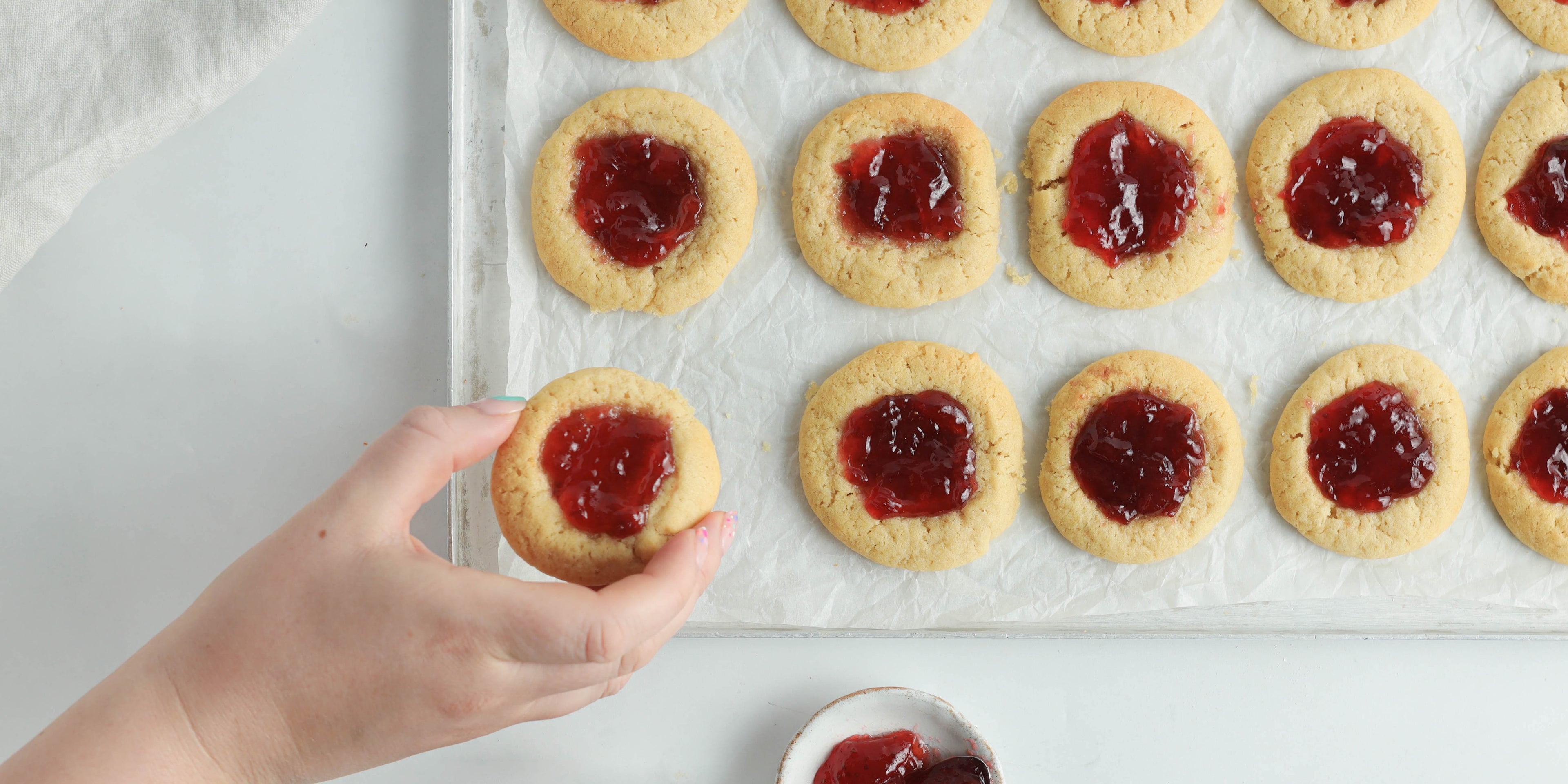 Tray of circular biscuits with jam on top and a hand reaching in to take one