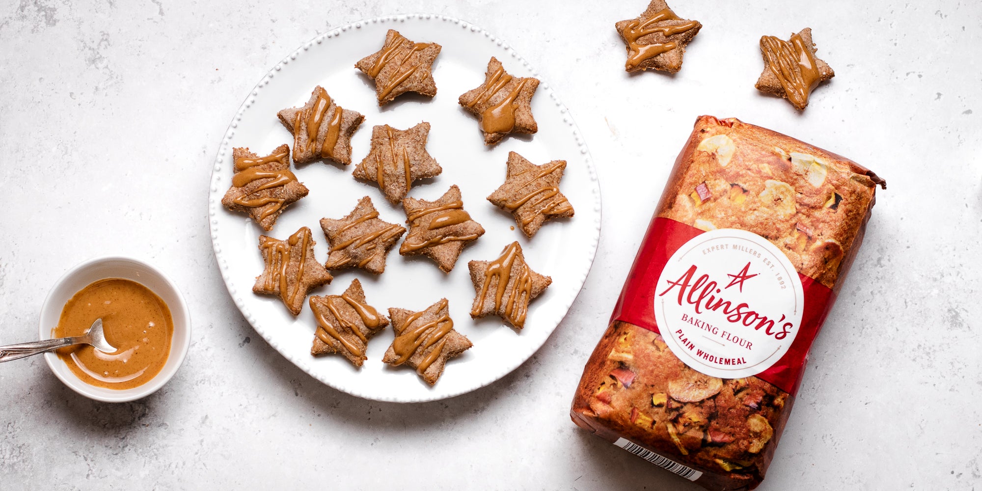 Dog Biscuits cut into festive stars and drizzled with peanut butter, next to a bag of Allinsons plain flour
