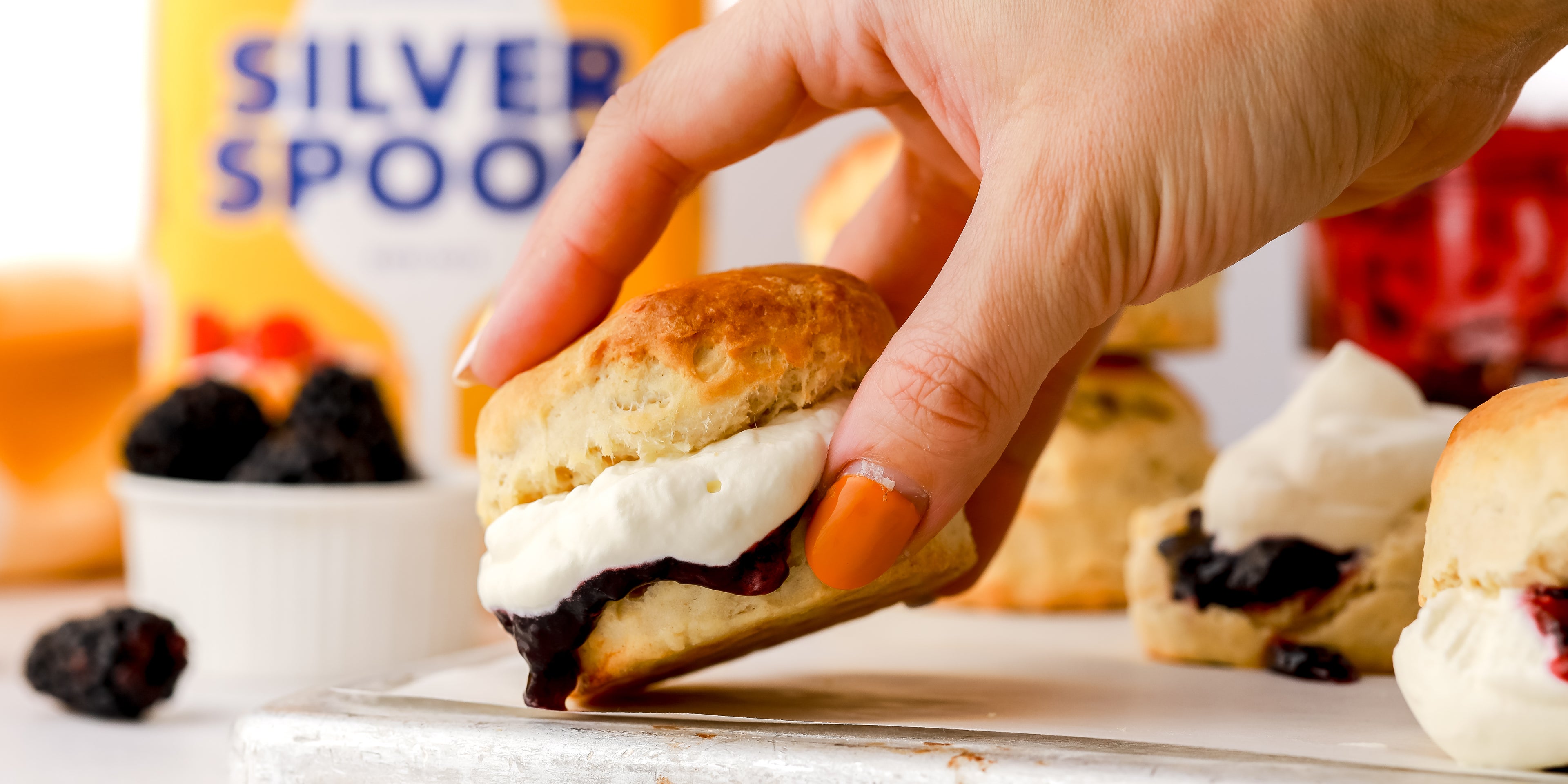 Hand reaching in to grab a scone with jam and cream