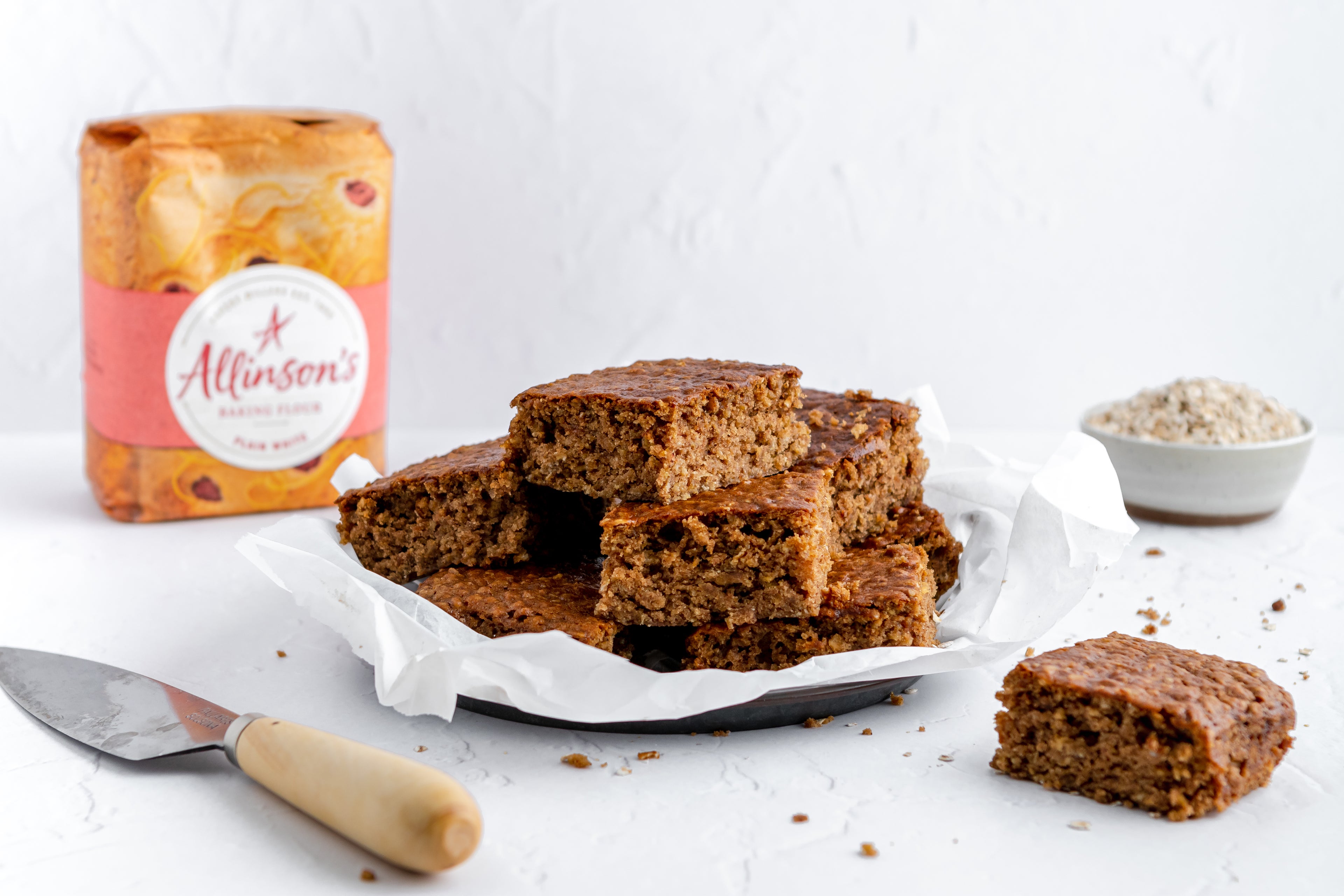 Sticky Yorkshire Parkin slices next to Allinson's Plain White flour, and a cake knife